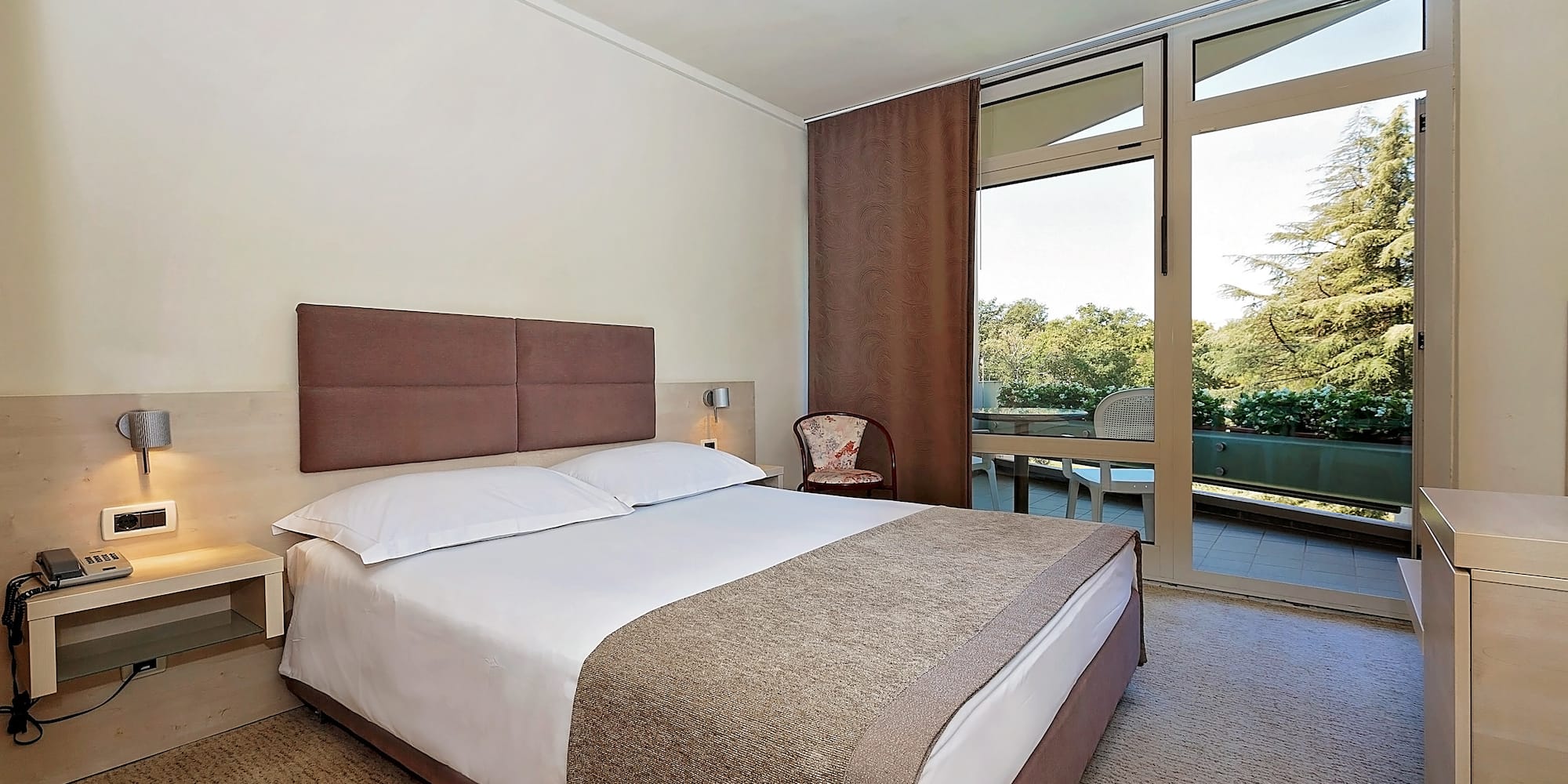 a bed with a brown headboard and a chair in a room with glass doors