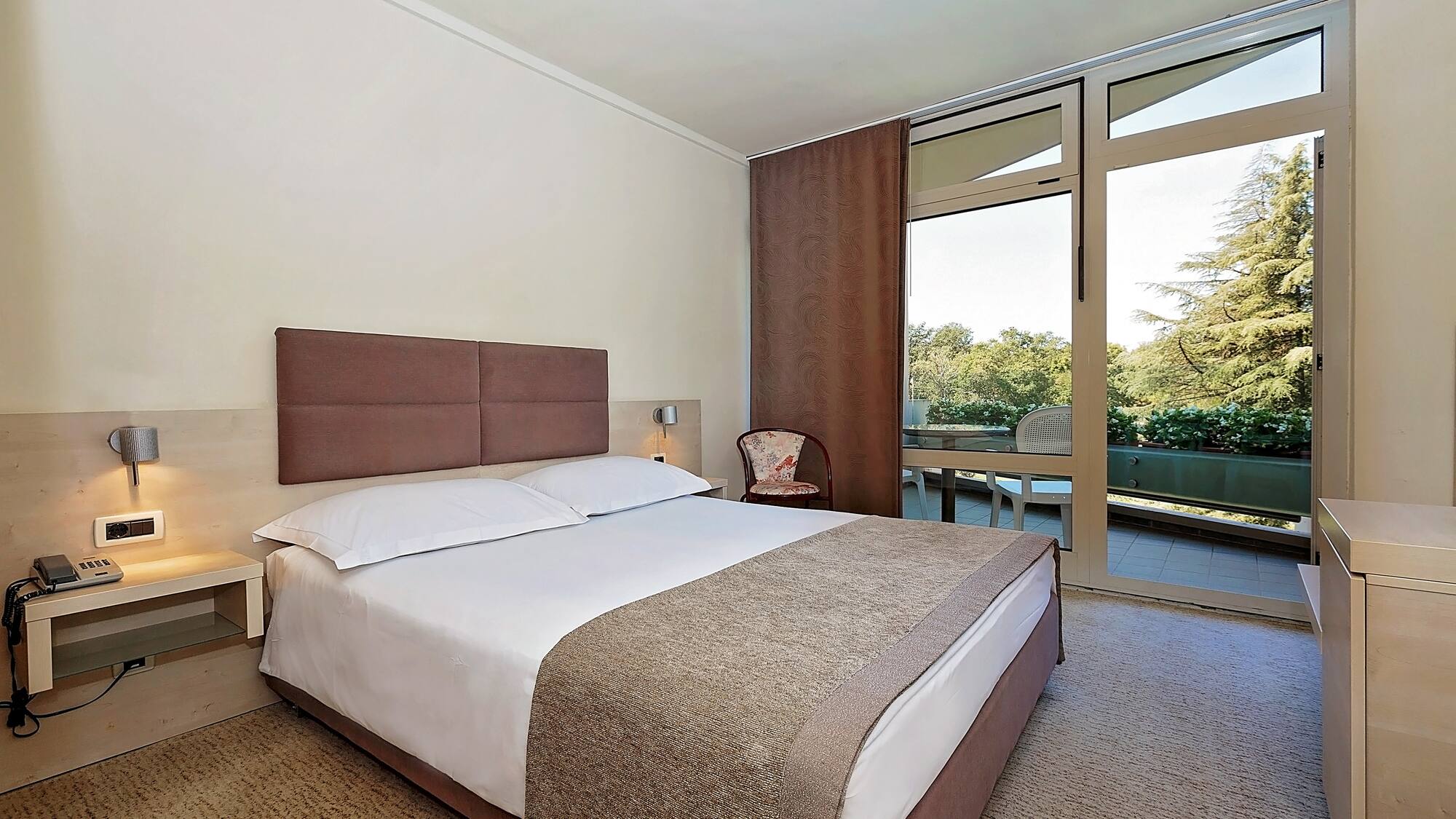 a bed with a brown headboard and a chair in a room with glass doors