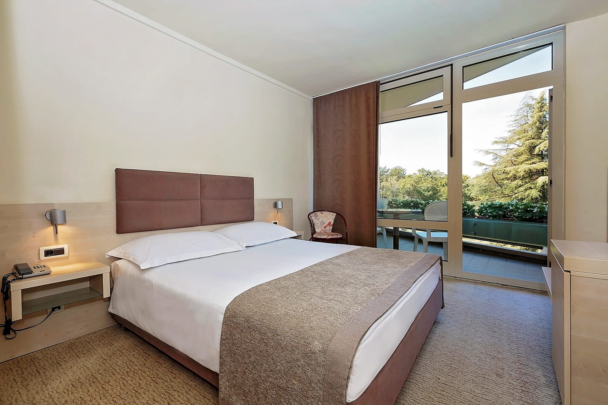 a bed with a brown headboard and a chair in a room with glass doors