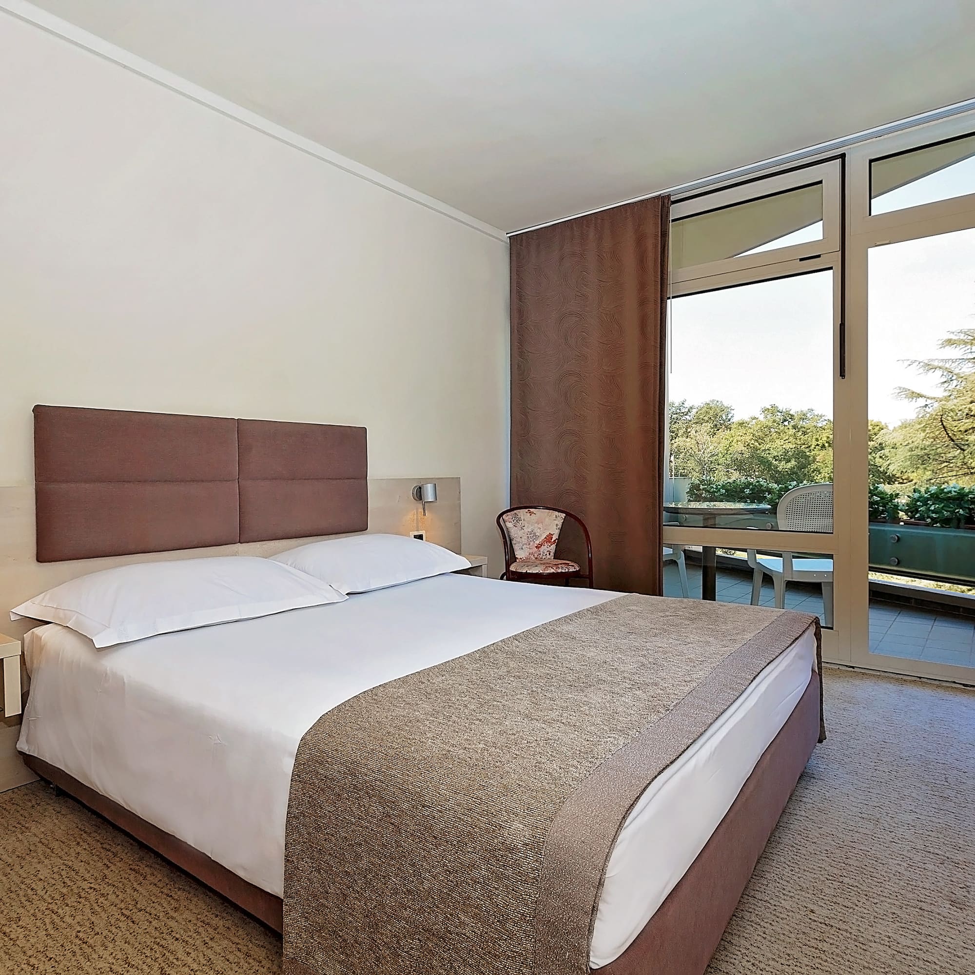a bed with a brown headboard and a chair in a room with glass doors