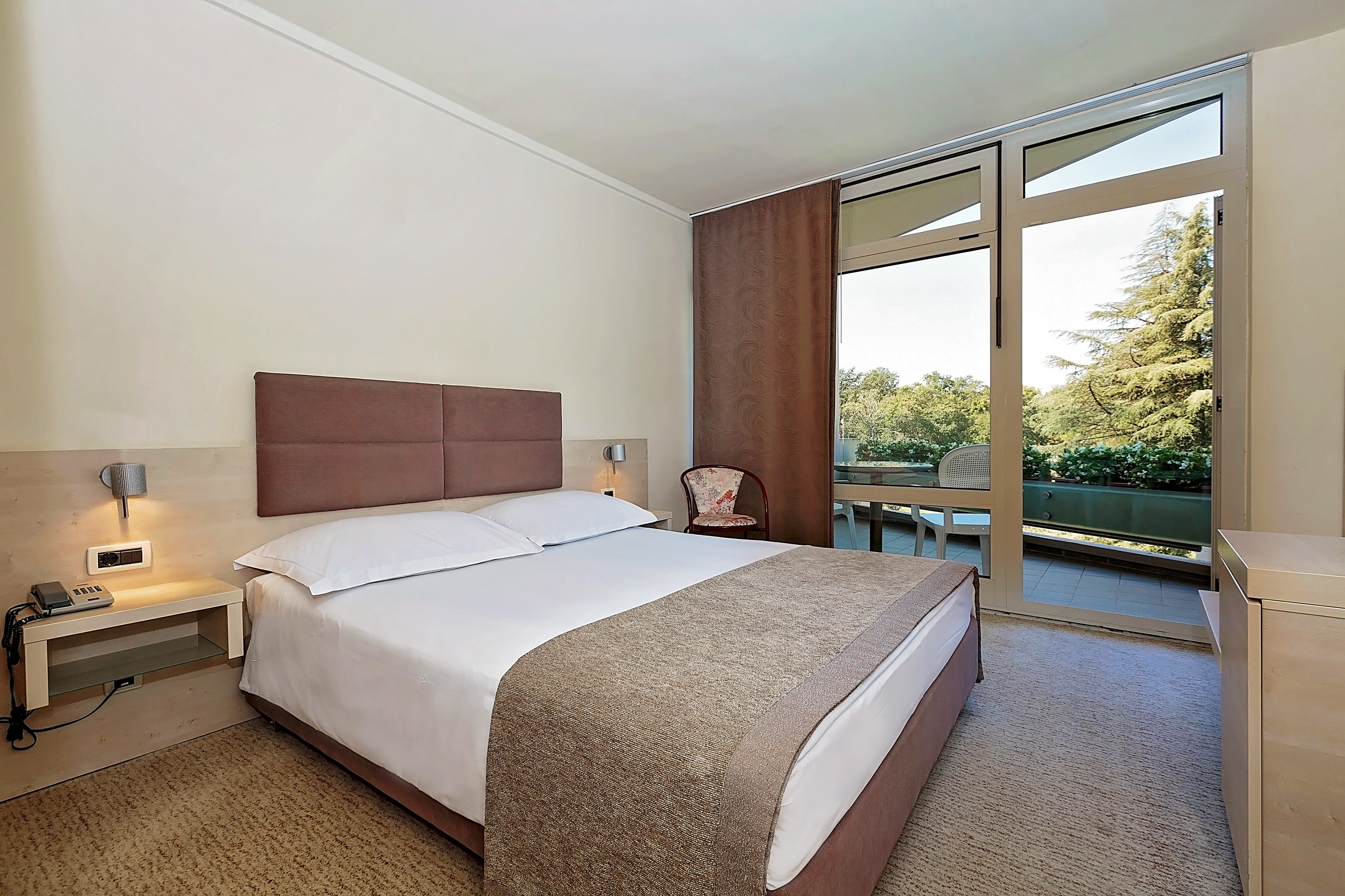 a bed with a brown headboard and a chair in a room with glass doors