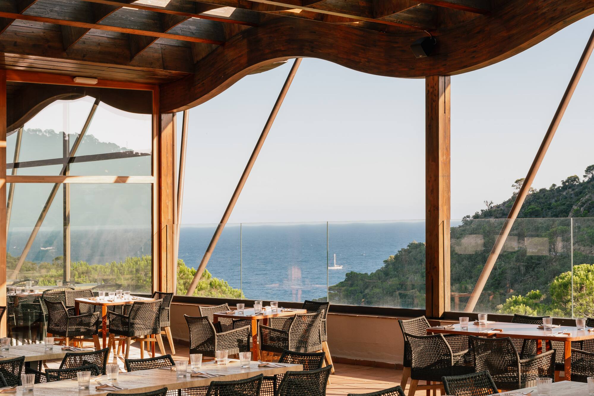 Ocean view restaurant terrace with wooden pergola, tables, and woven chairs.