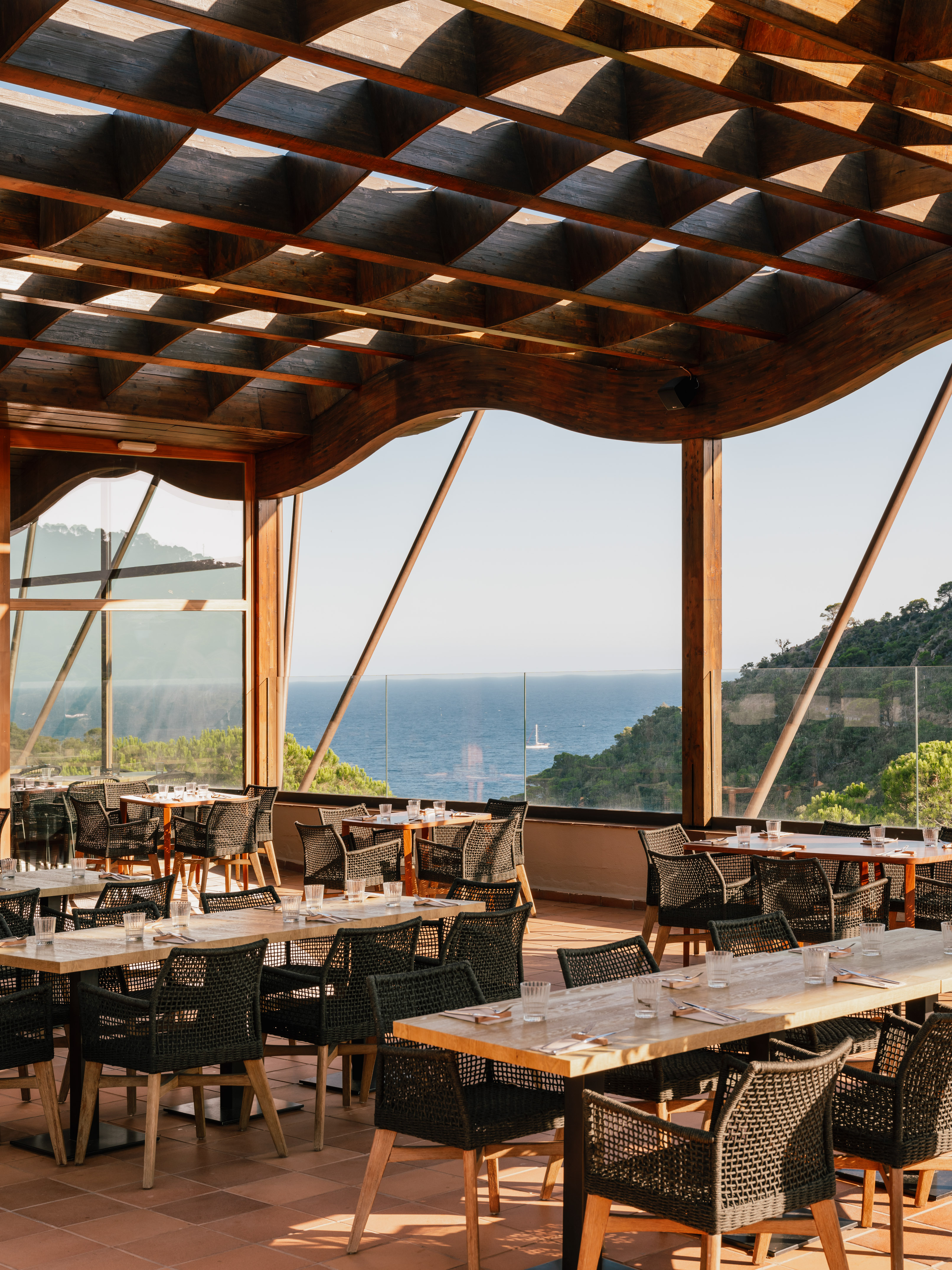 Ocean view restaurant terrace with wooden pergola, tables, and woven chairs.