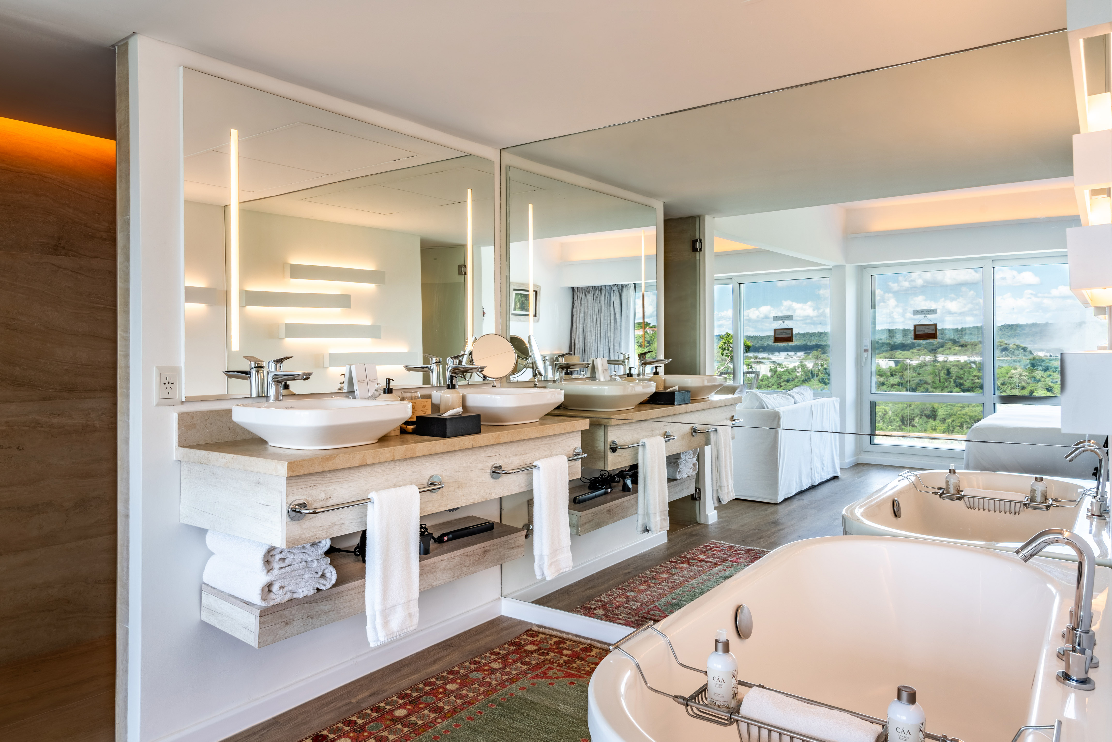 Luxury hotel bathroom with double vanity, two tubs, and scenic window views.