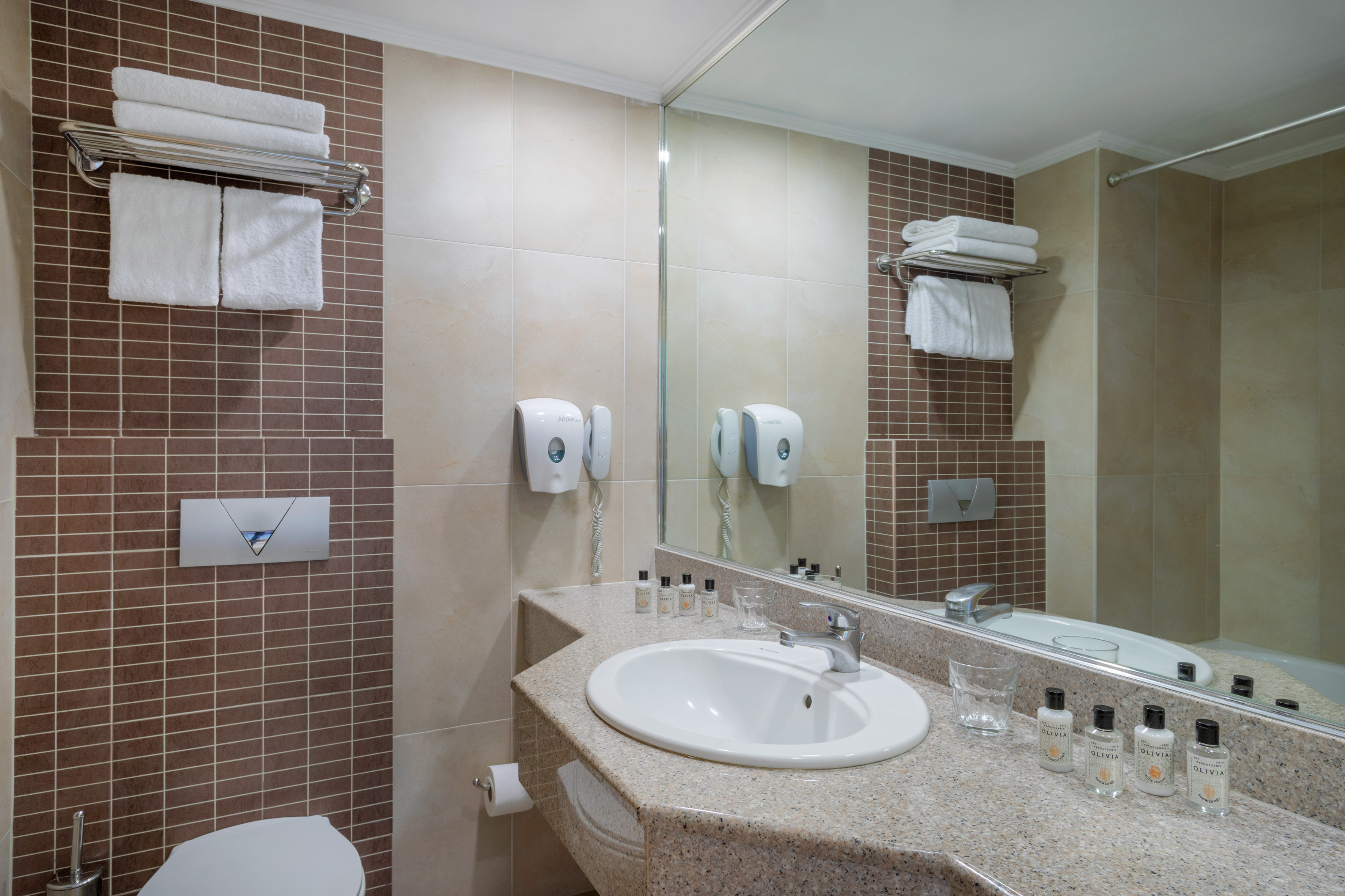 Modern hotel bathroom with sink, mirror, white towels, and tiled walls.