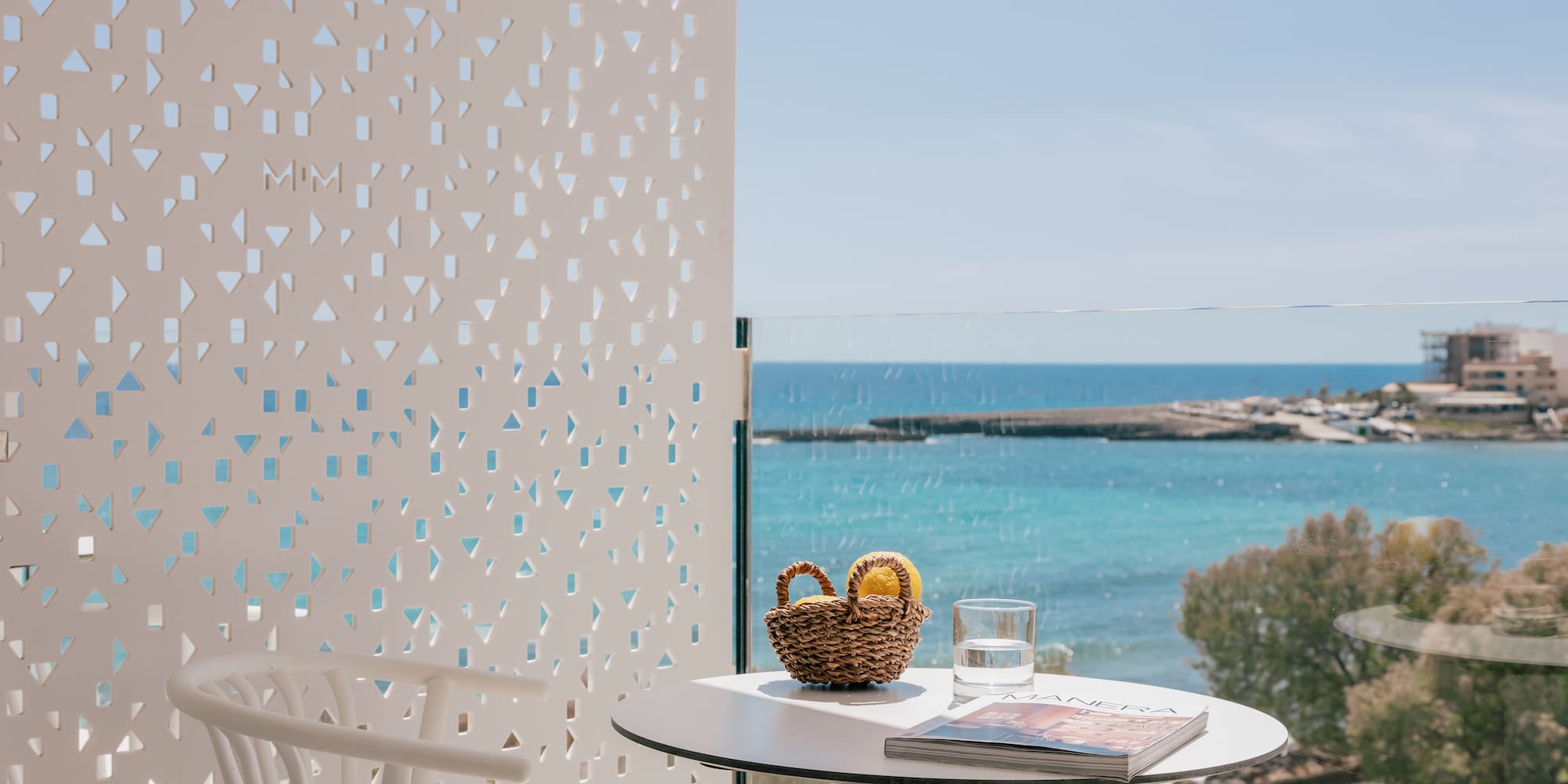 Sea view balcony with white table, lemons, magazine, and geometric screen.