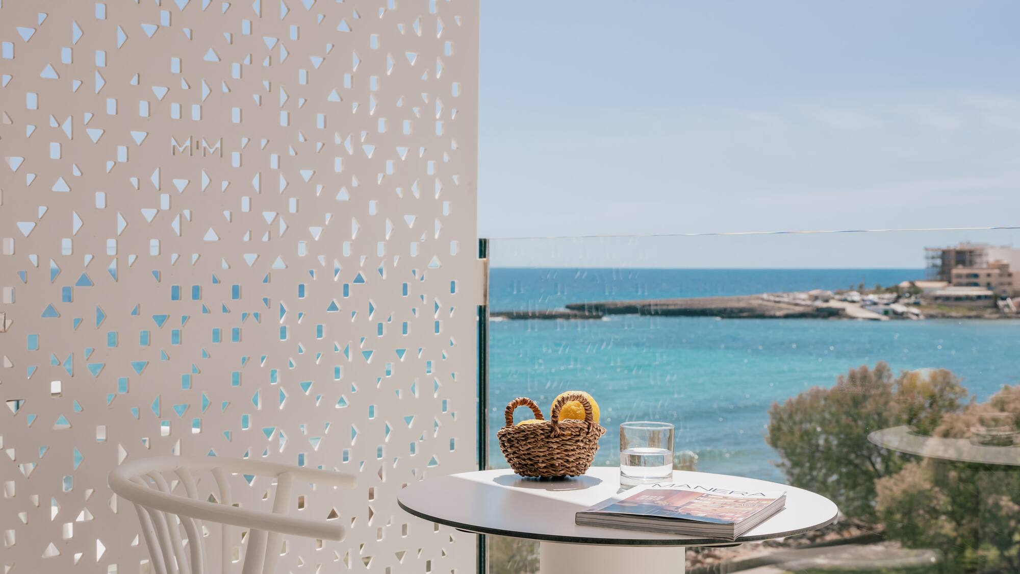 Sea view balcony with white table, lemons, magazine, and geometric screen.