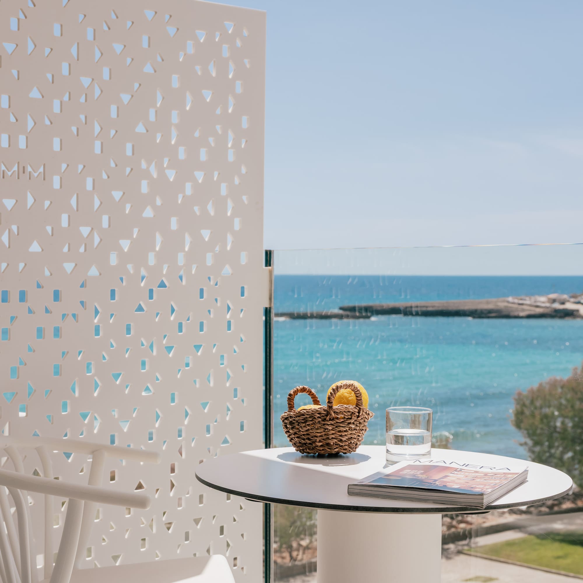 Sea view balcony with white table, lemons, magazine, and geometric screen.