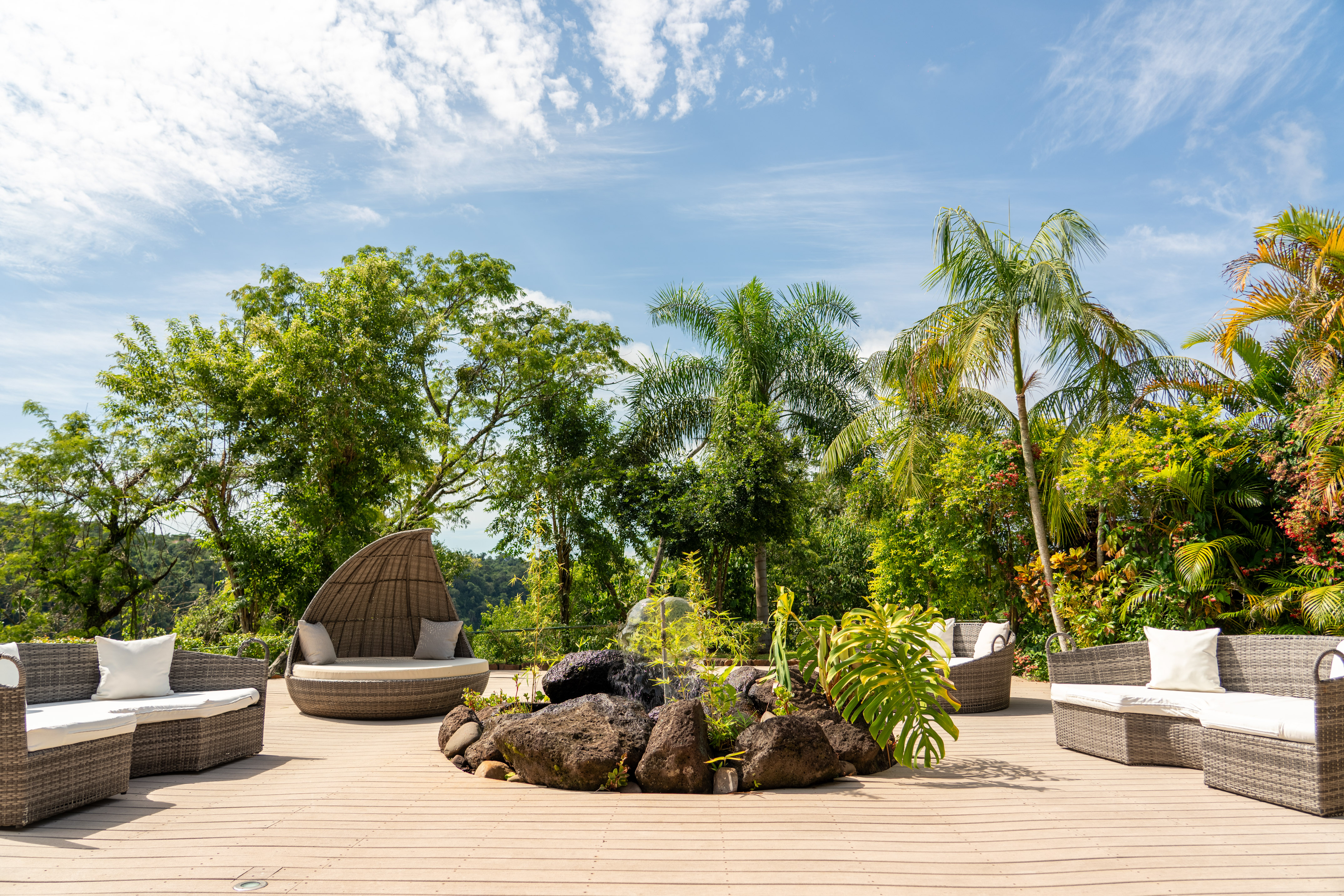 Tropical outdoor patio with wicker furniture, rock water feature, and lush garden.