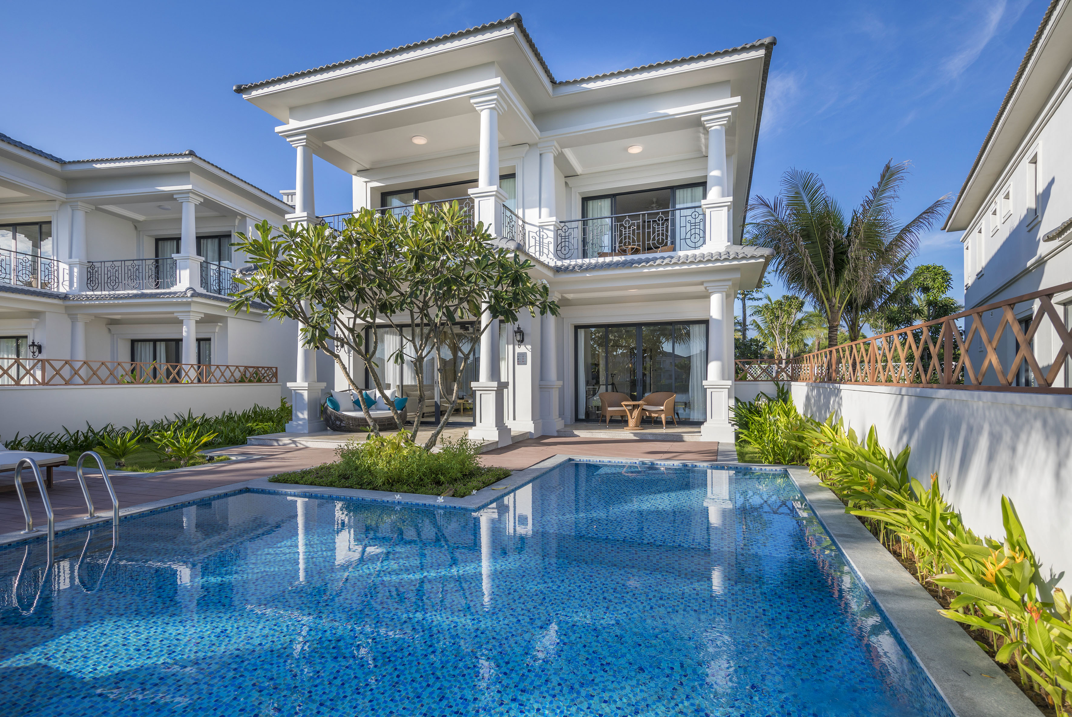 Modern white luxury villa with private pool, tropical garden, and blue sky.