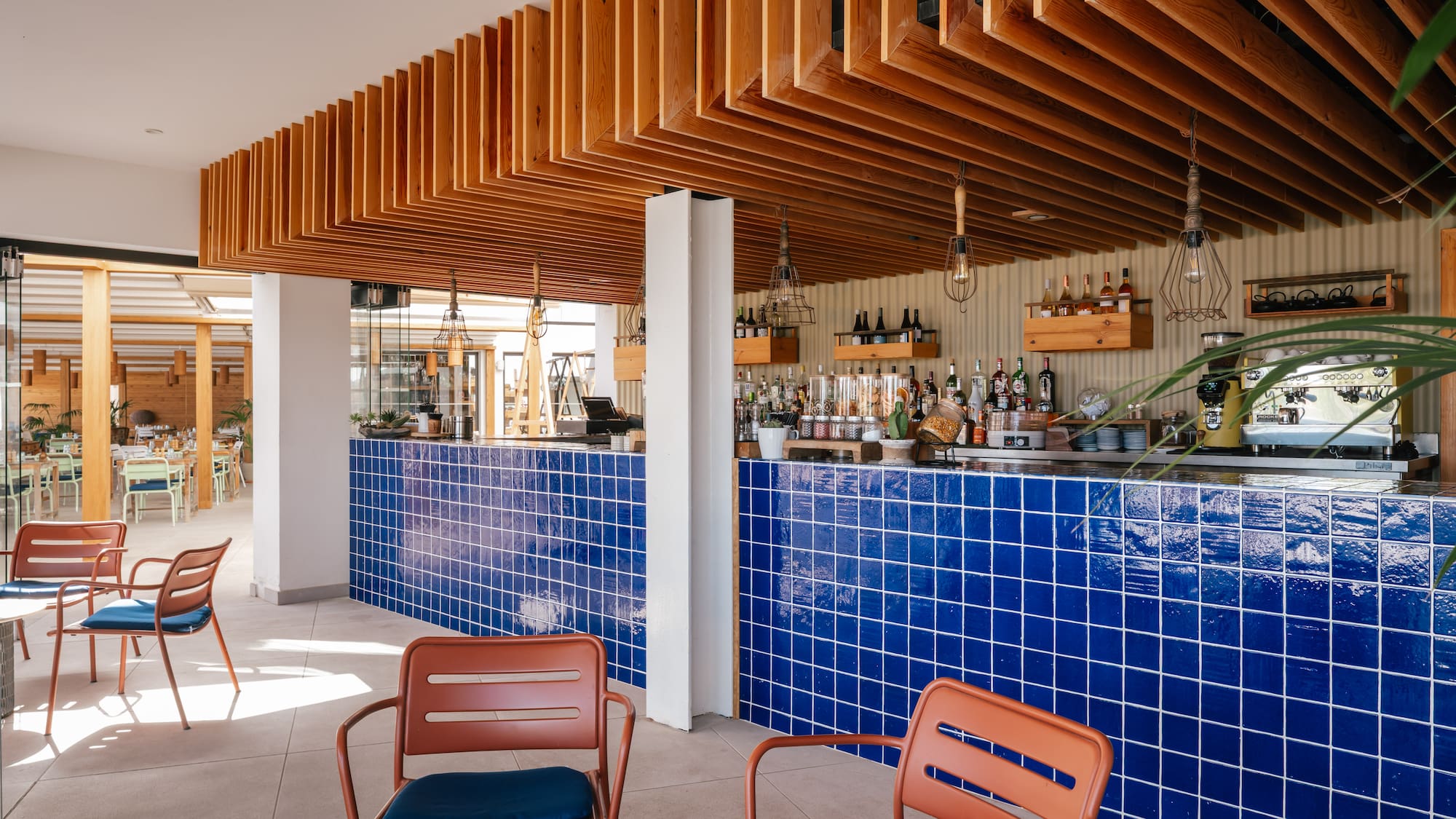 Modern cafe bar interior with blue tiled counter, wooden ceiling, and seating.