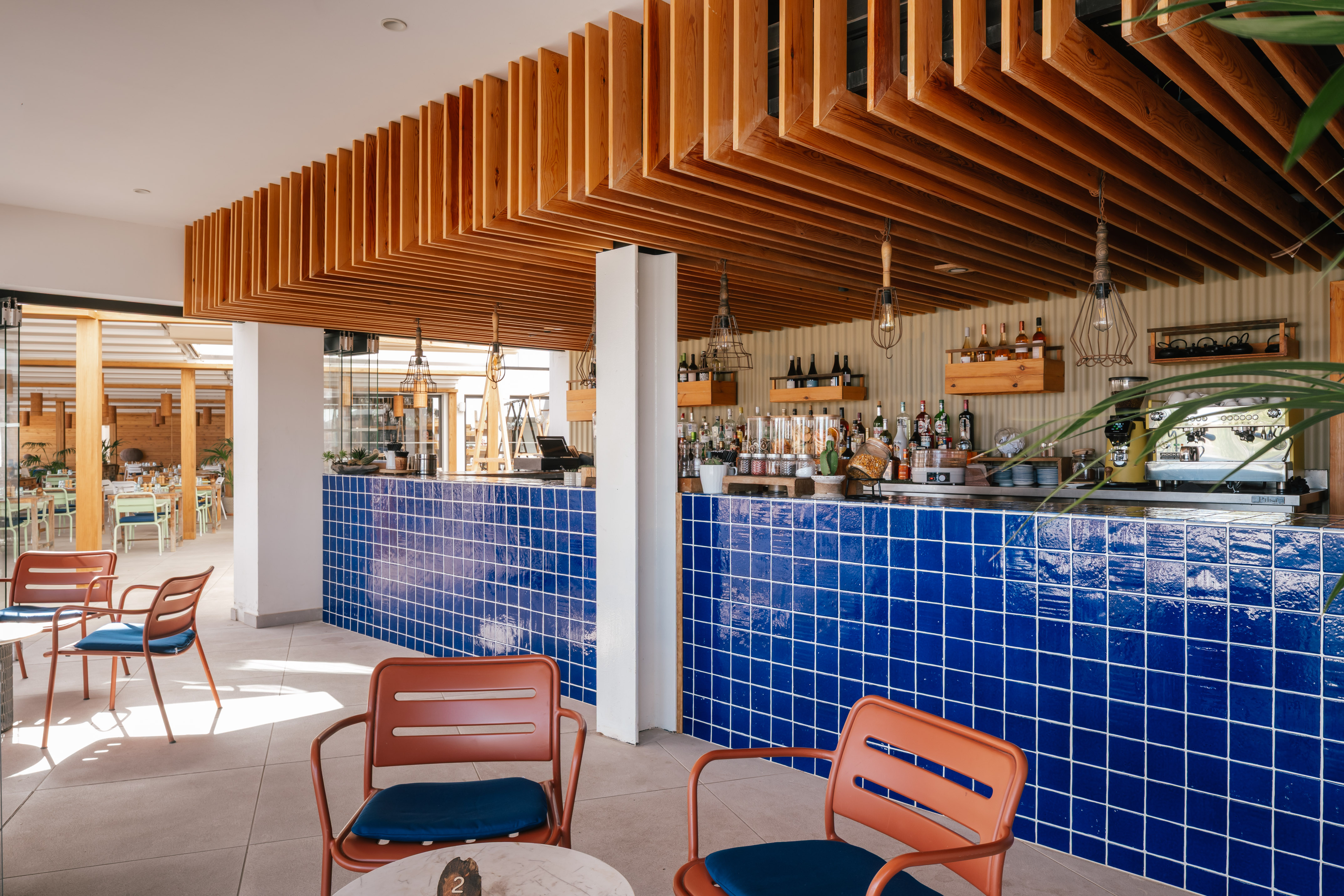 Modern cafe bar interior with blue tiled counter, wooden ceiling, and seating.
