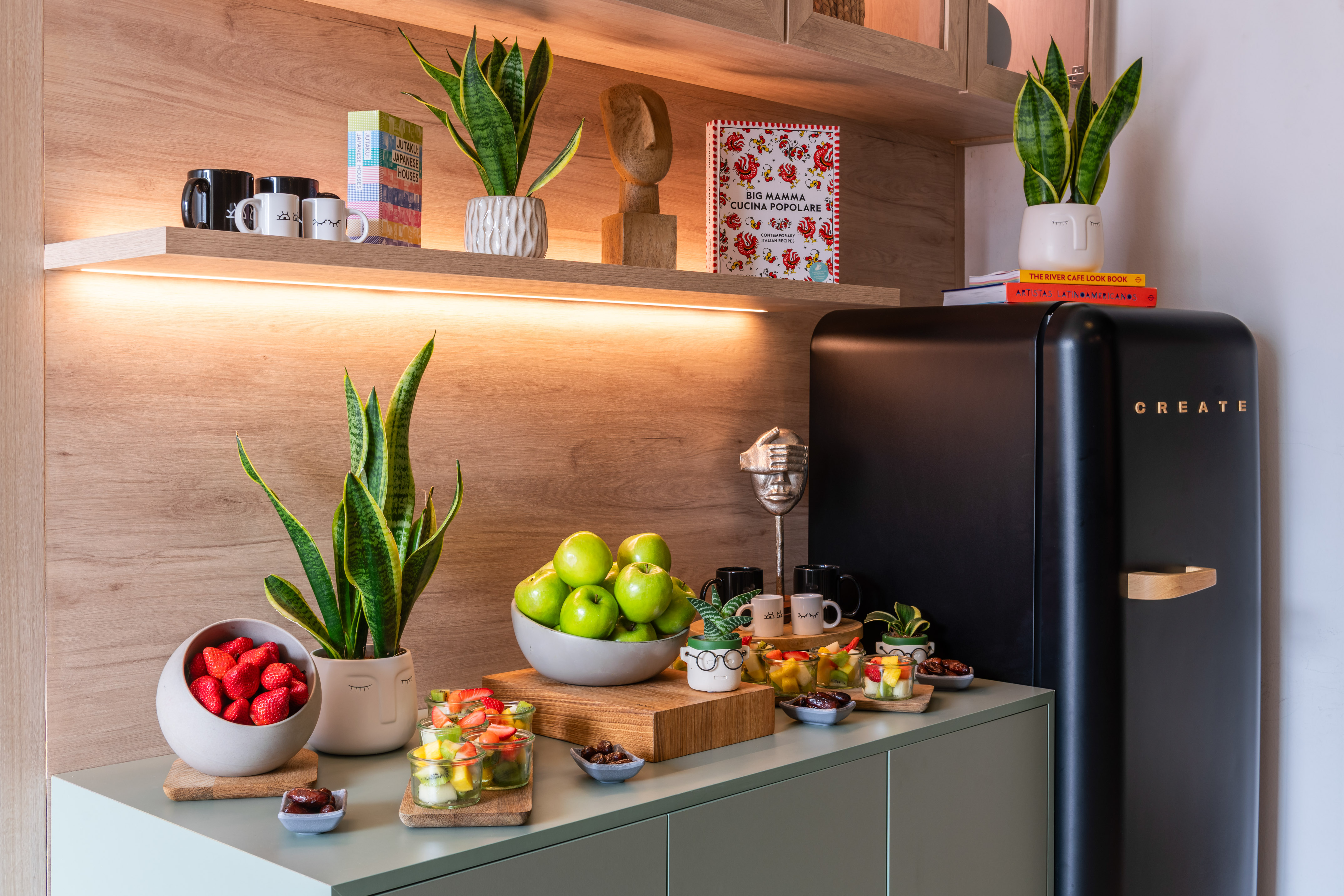 Modern kitchen with black retro fridge, fresh fruit, and potted plants.