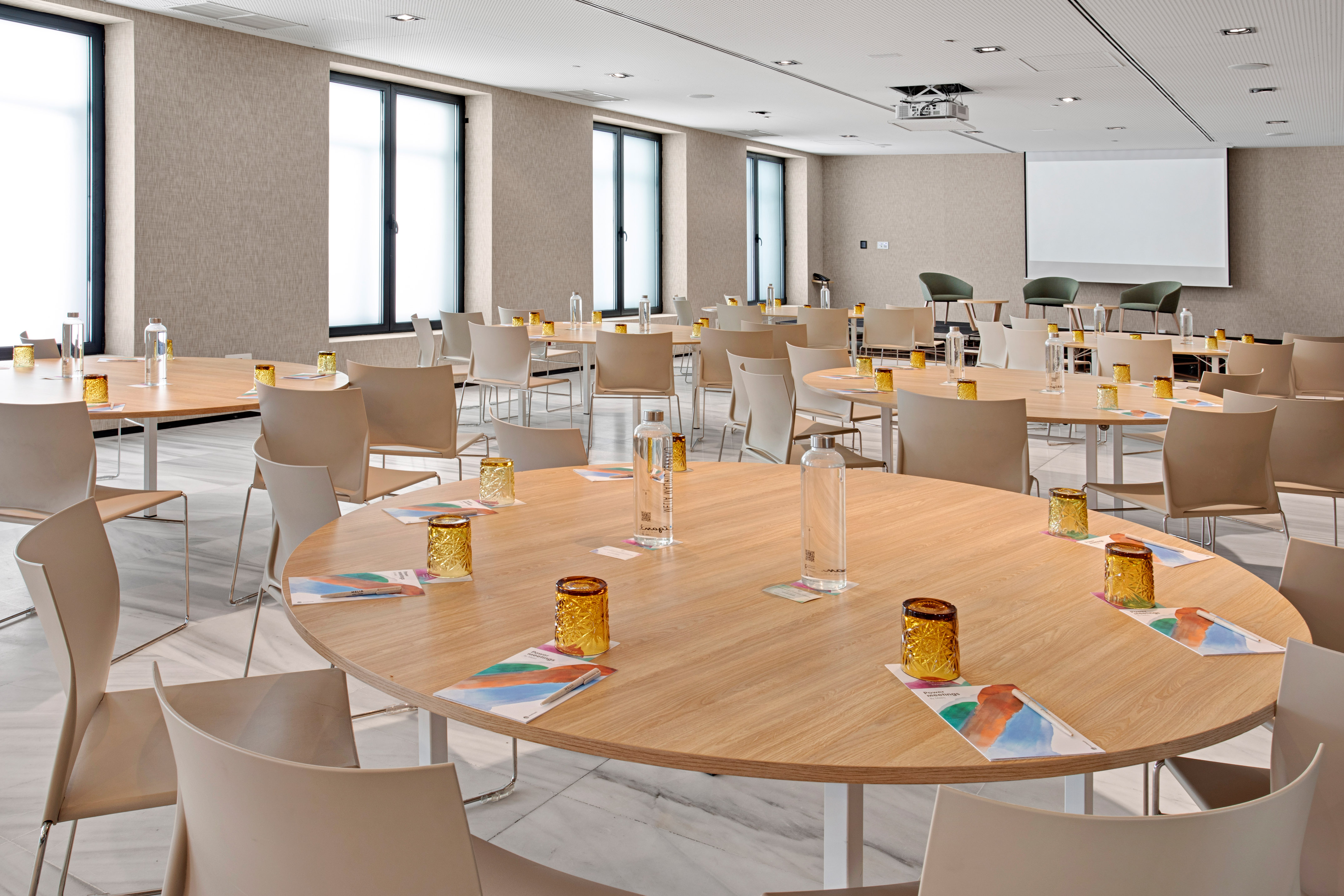 Modern meeting room with round tables, presentation screen, and bright windows.