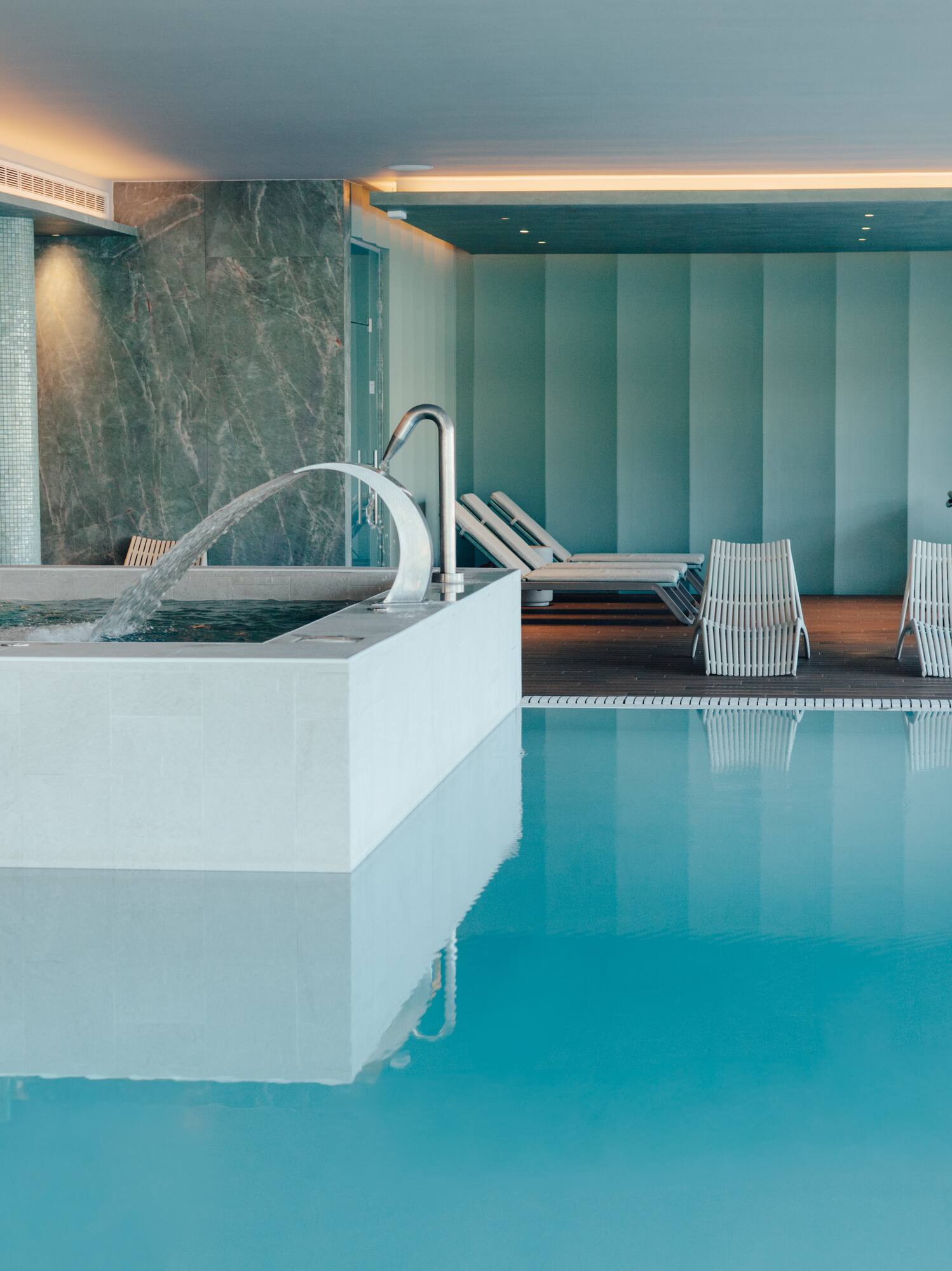 Indoor spa pool with jacuzzi, water jet, and lounge chairs.