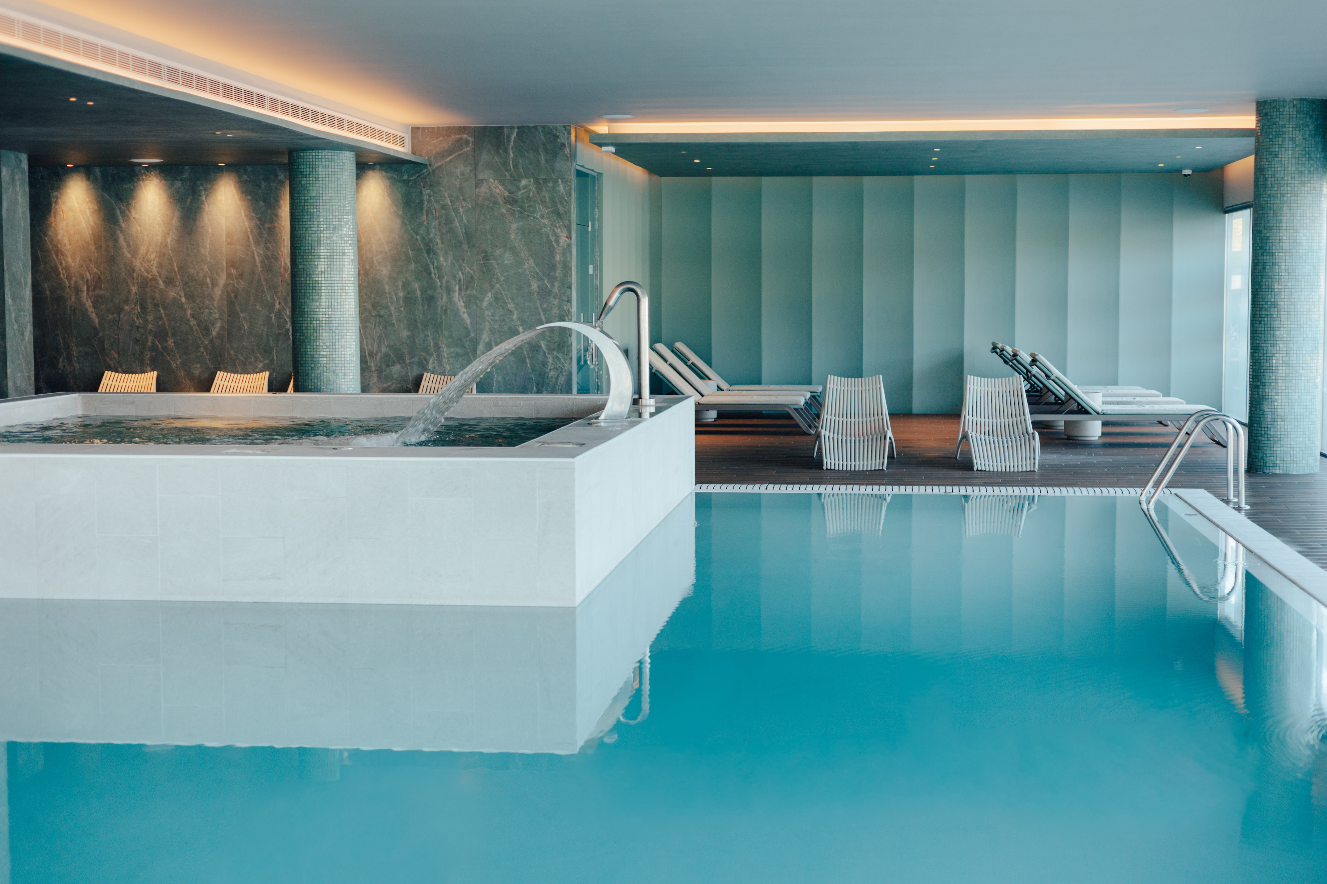 Indoor spa pool with jacuzzi, water jet, and lounge chairs.