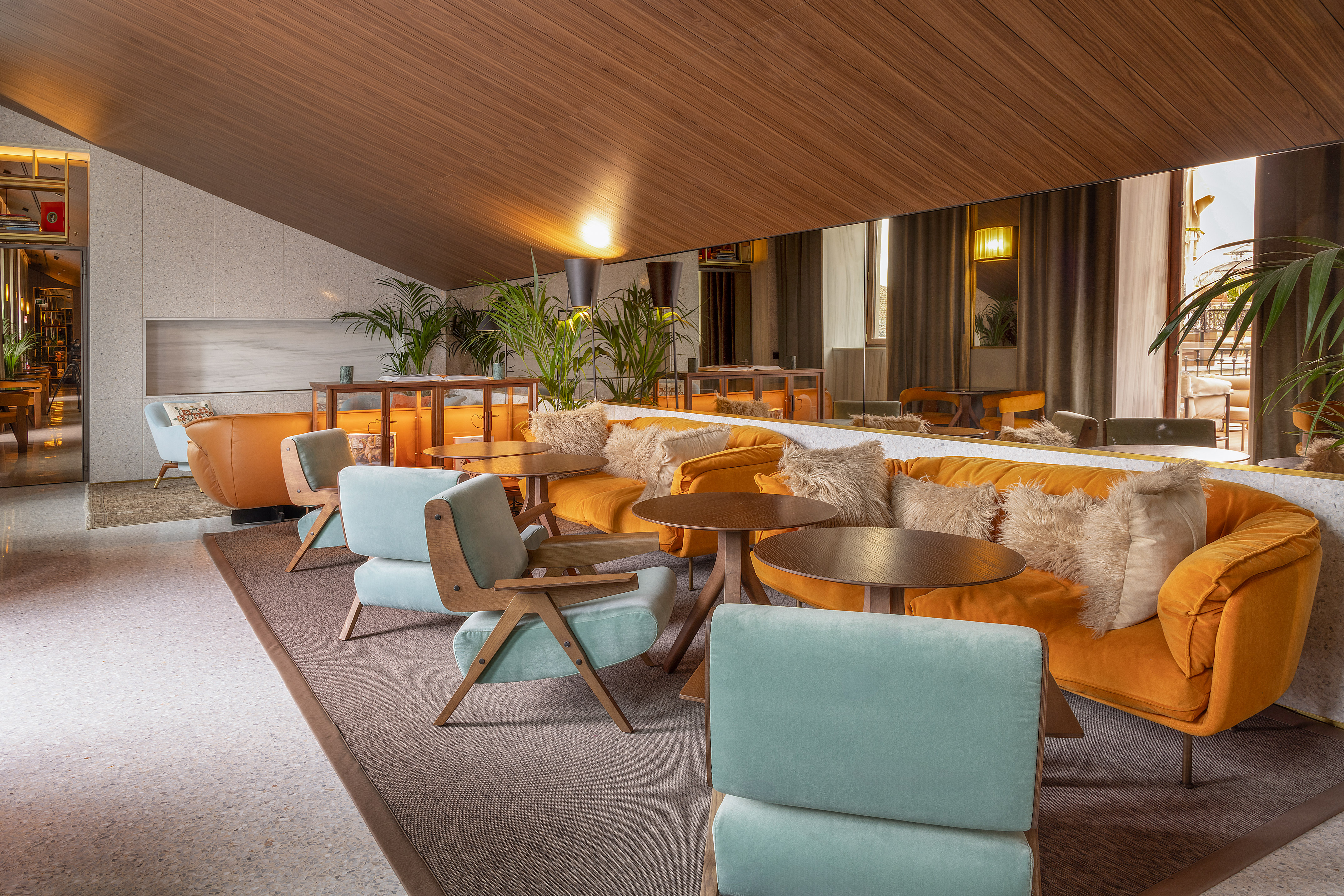 Stylish hotel lounge with orange sofas, blue armchairs, and wood ceiling.