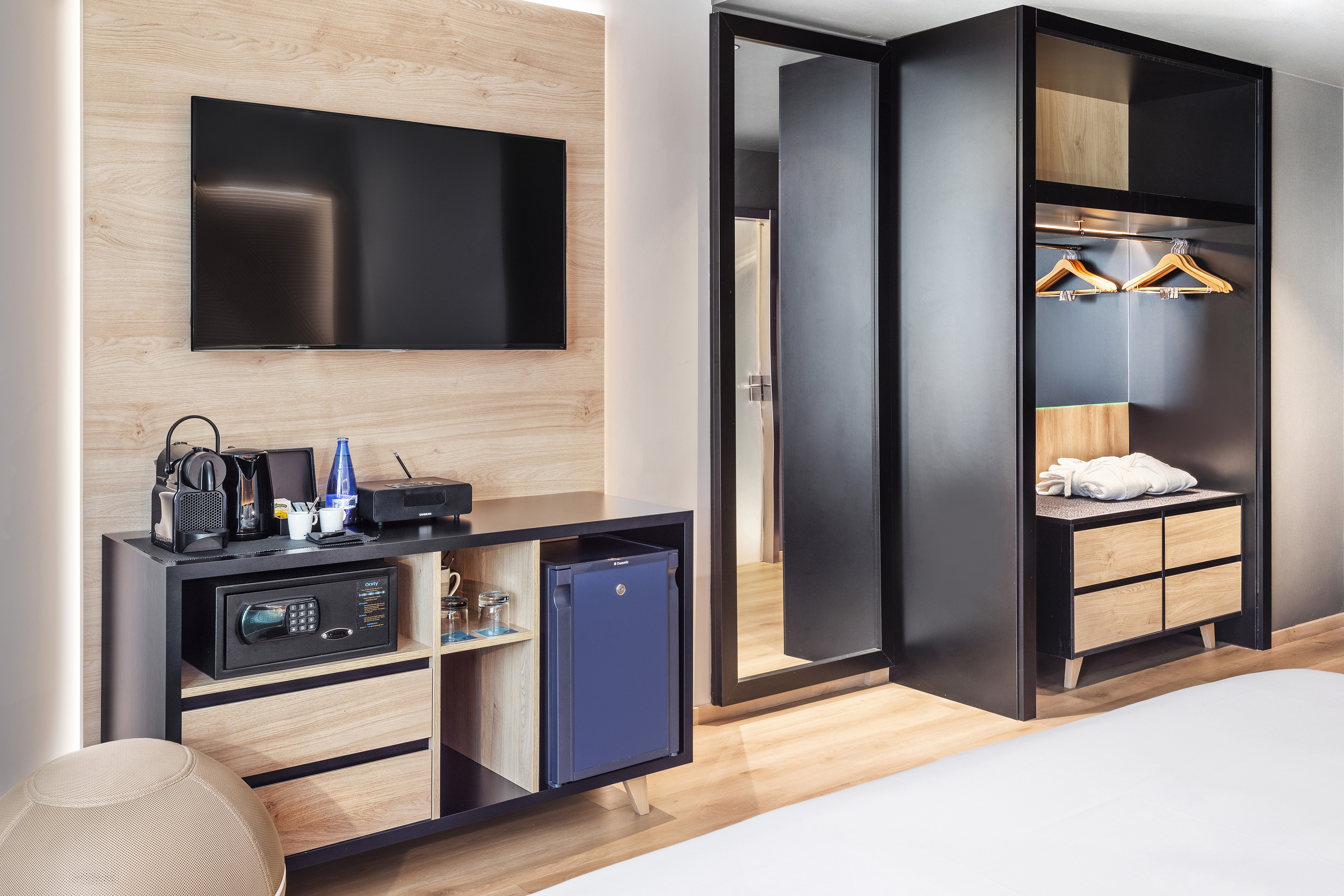 Modern hotel room with TV, minibar, safe, coffee machine, and open wardrobe.