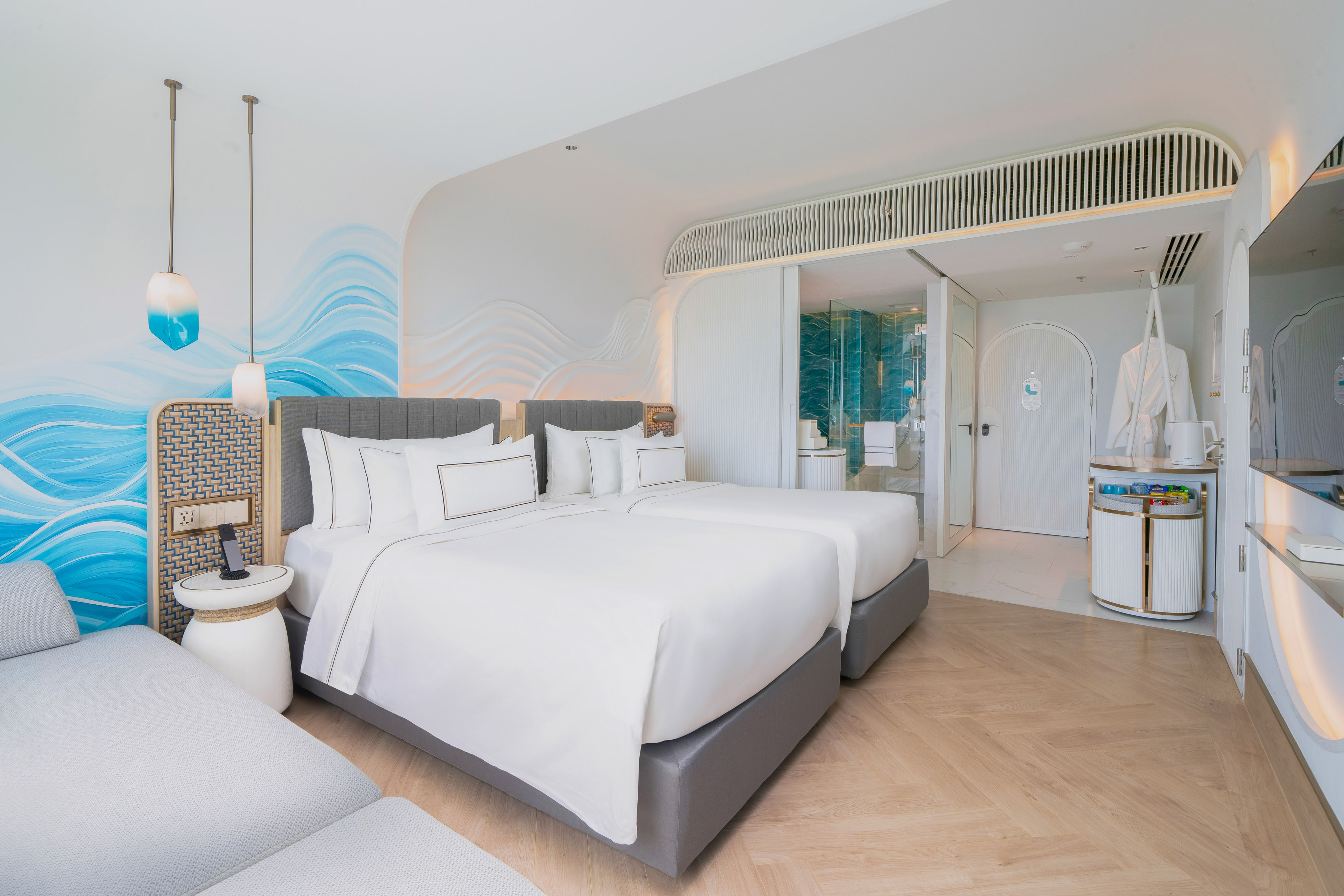 Coastal-themed hotel room with twin beds, blue wave decor, and modern bathroom.
