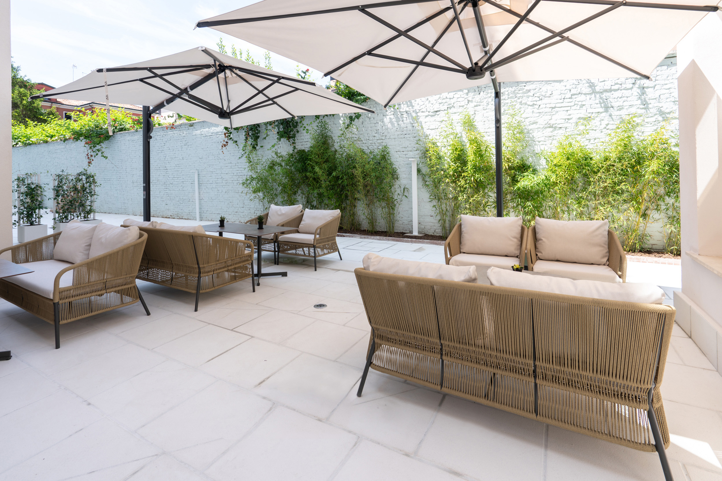 Outdoor patio lounge with modern rope sofas, white umbrellas, and green bamboo.