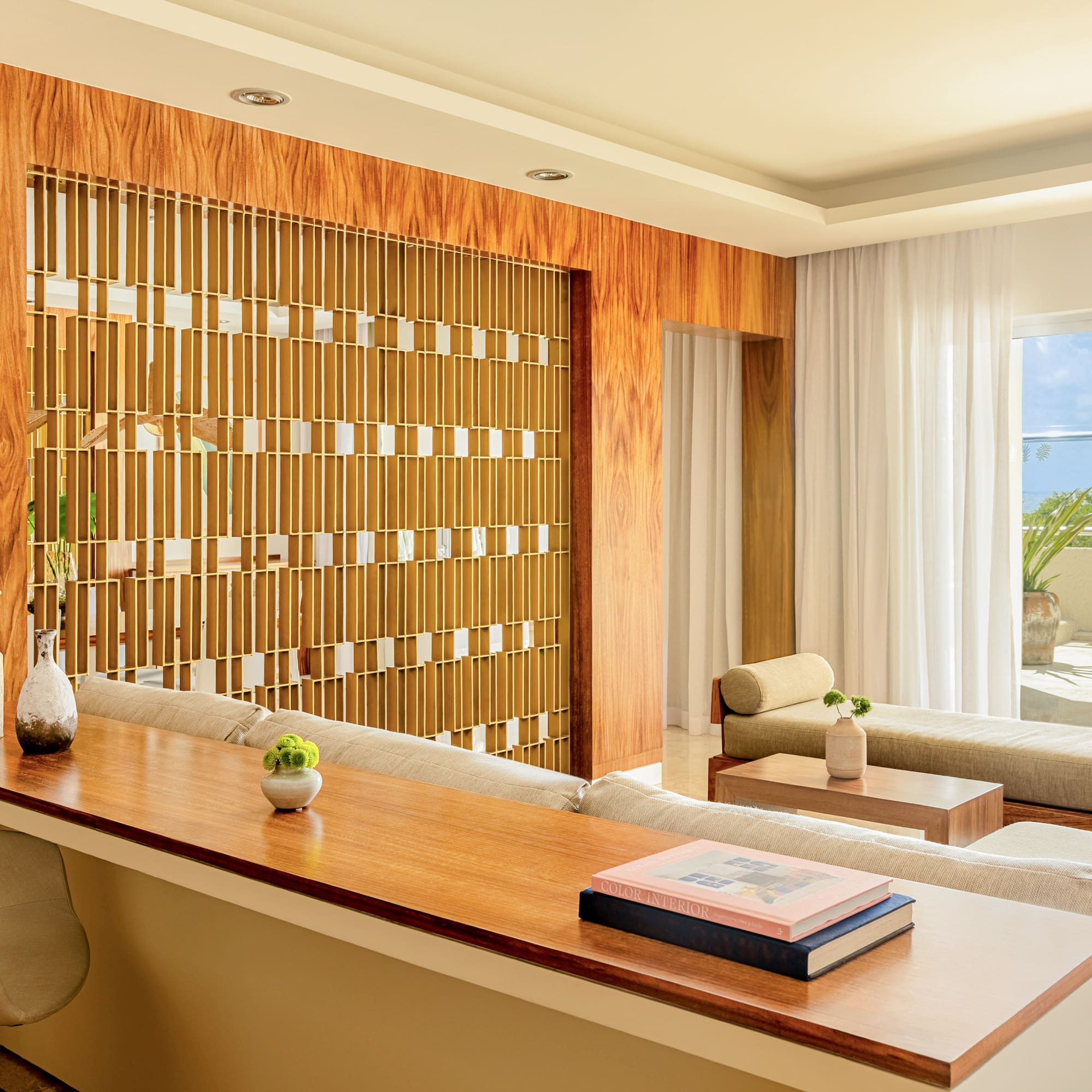 Modern living room with wood panels, decorative divider, lounge sofas, and patio view.