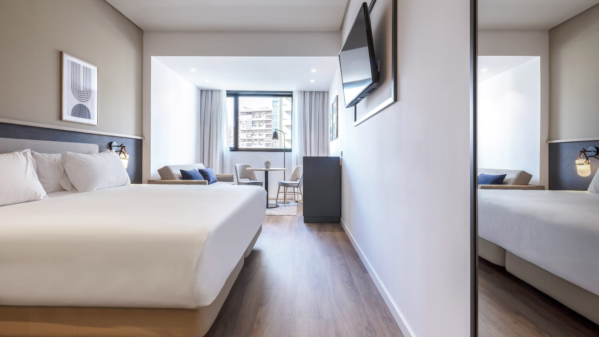 Modern hotel room with large bed, TV, hardwood floor, and dining area.