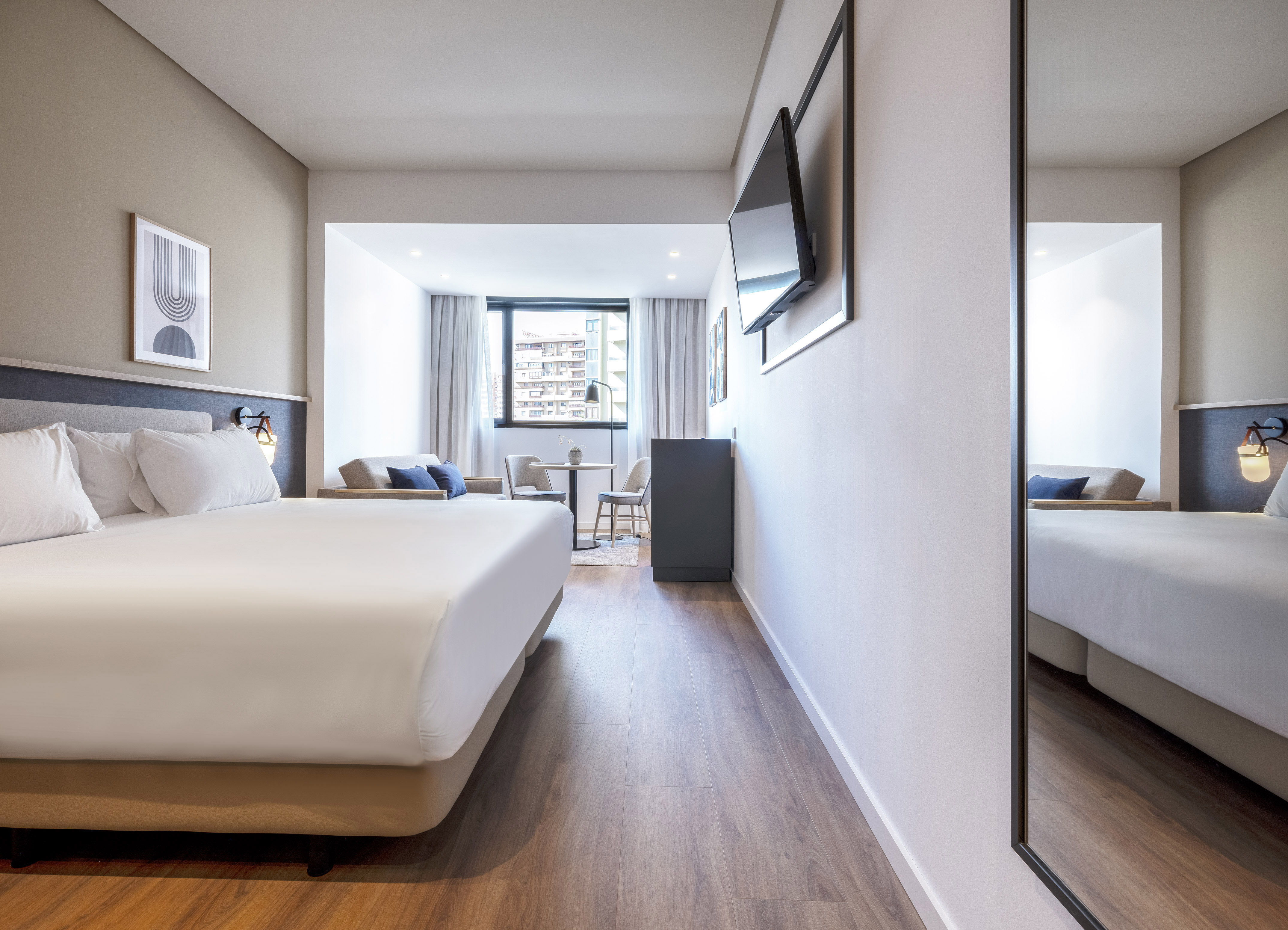 Modern hotel room with large bed, TV, hardwood floor, and dining area.