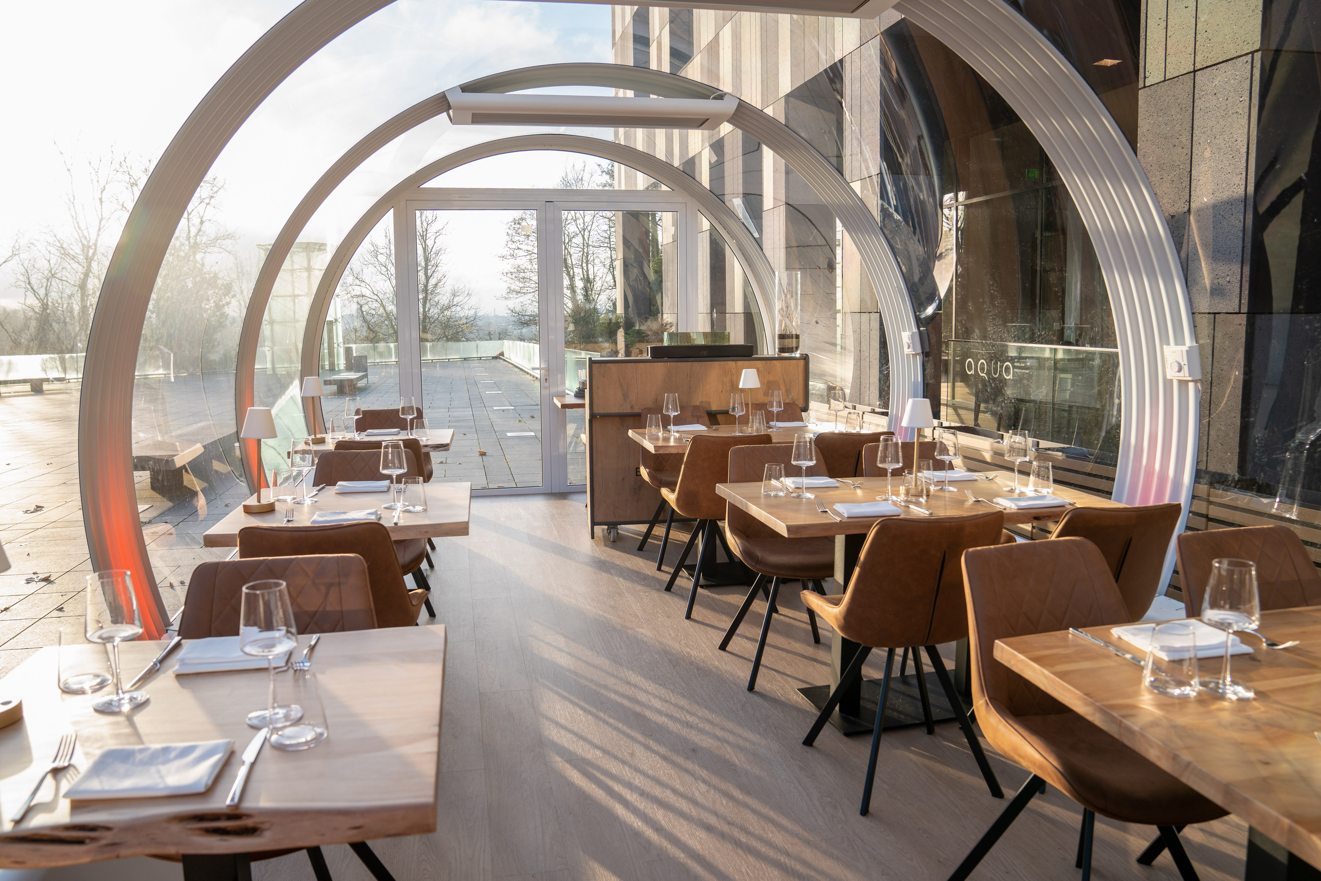 Bright restaurant dining area, glass arches, modern tables, brown chairs.