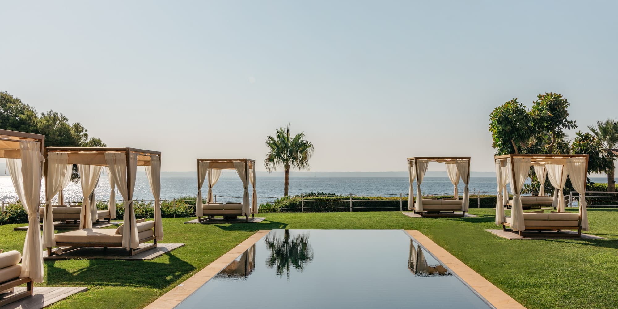 a pool with beds and a body of water in the background.