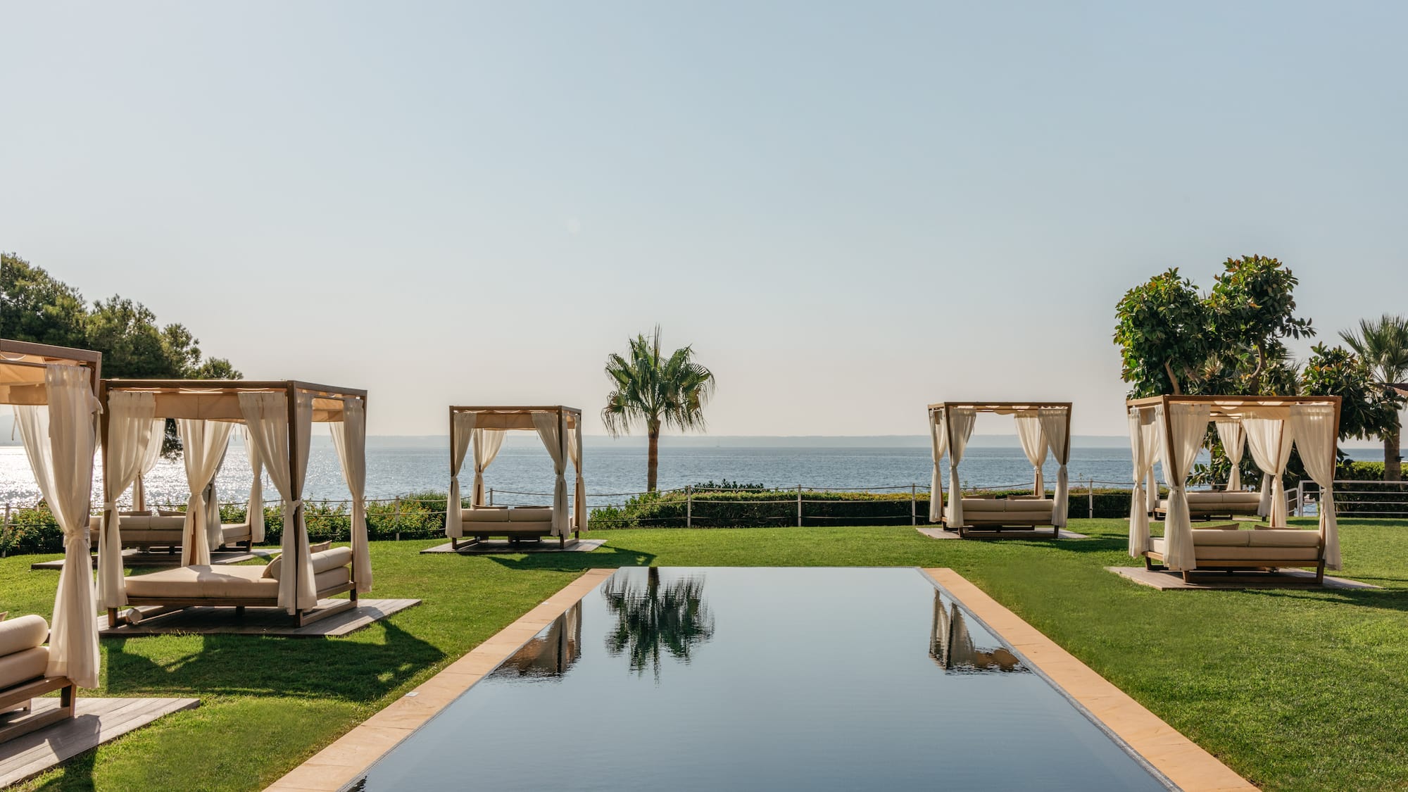 Oceanfront resort with infinity pool, lush lawn, and private cabana daybeds.