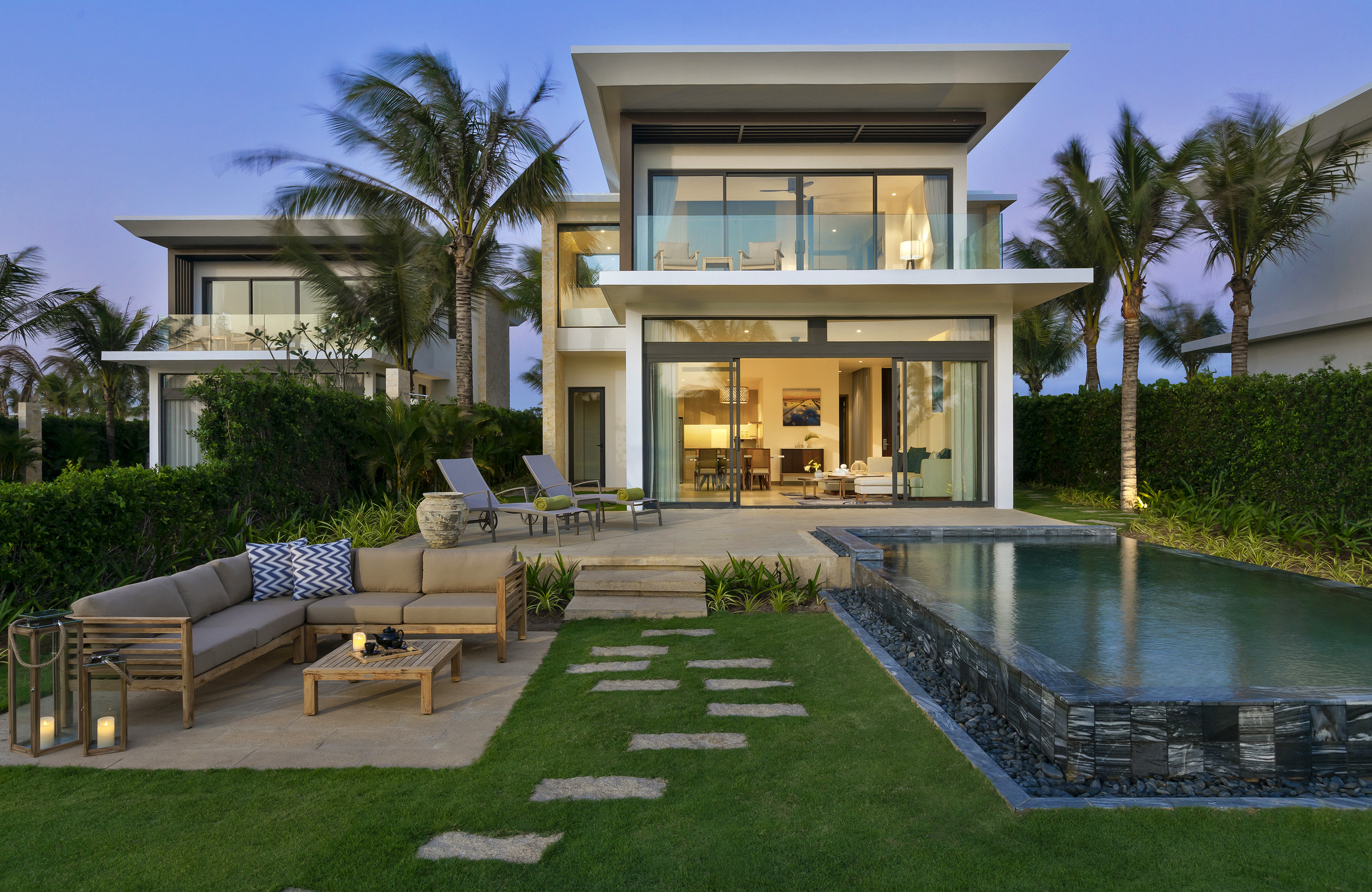 Modern tropical villa with private pool, outdoor patio, and lush garden at dusk.