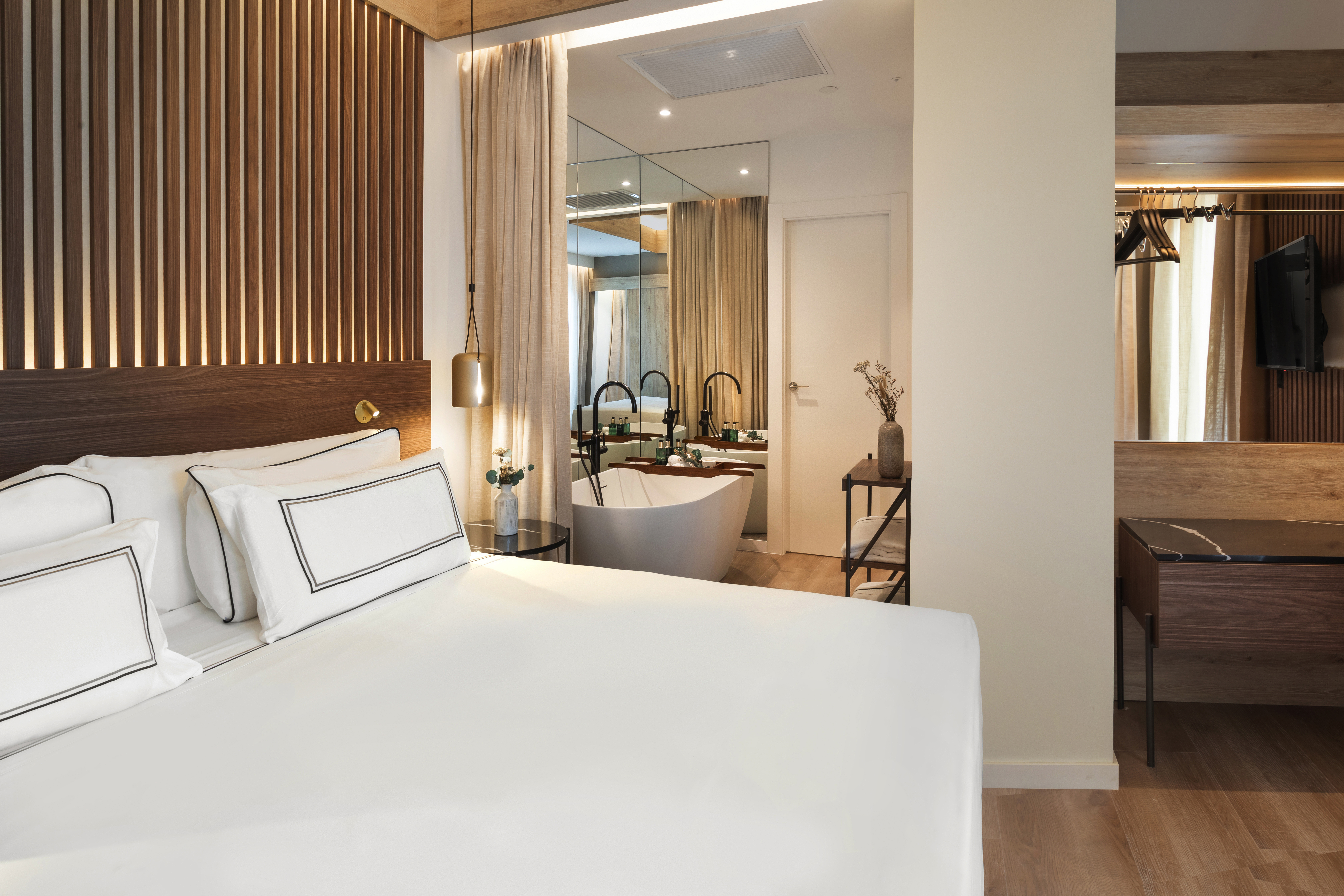 Modern hotel room: bed, wood accent wall, freestanding bathtub.