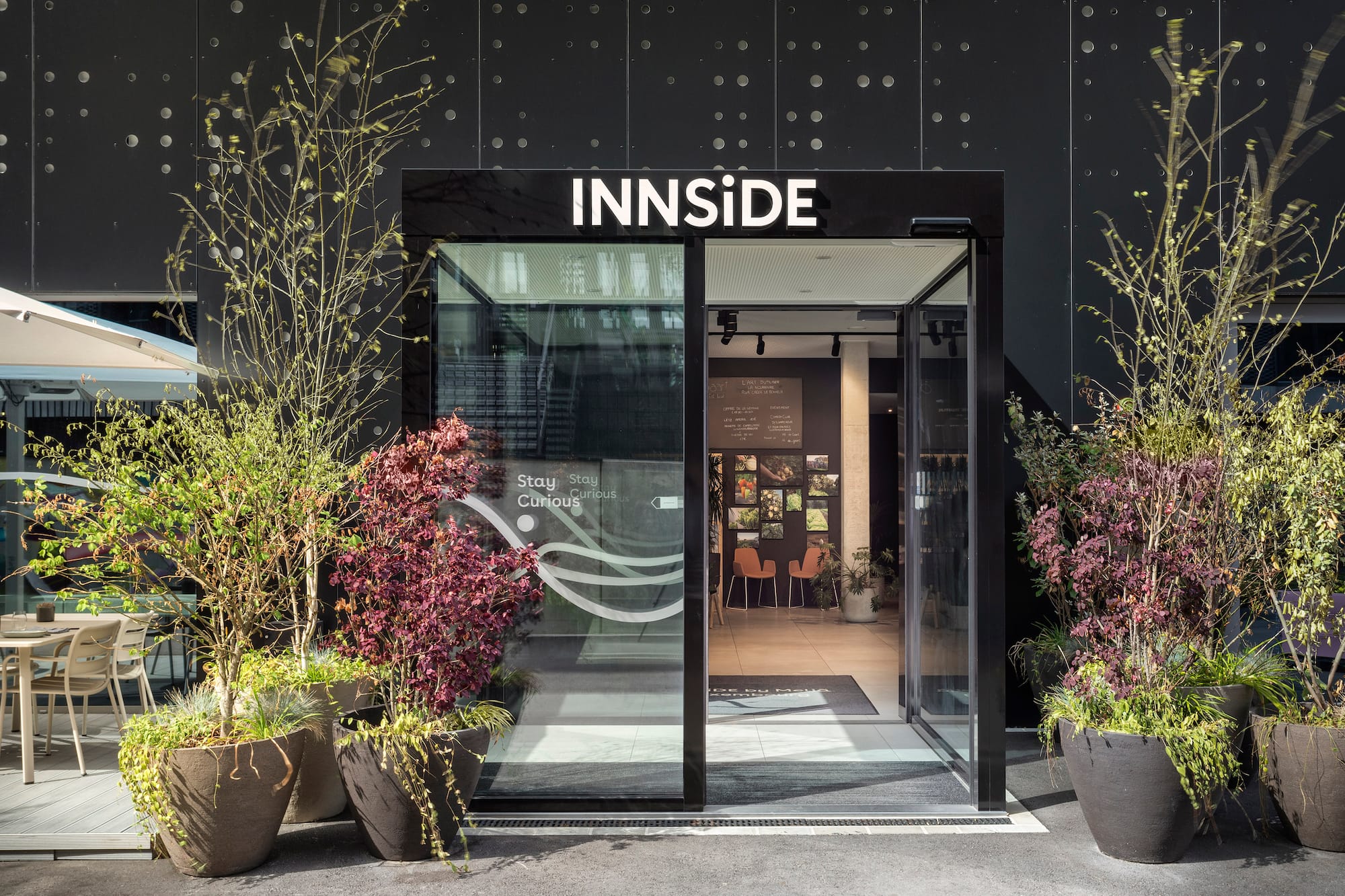 INNSIDE hotel entrance: modern glass doors, black facade, potted plants.
