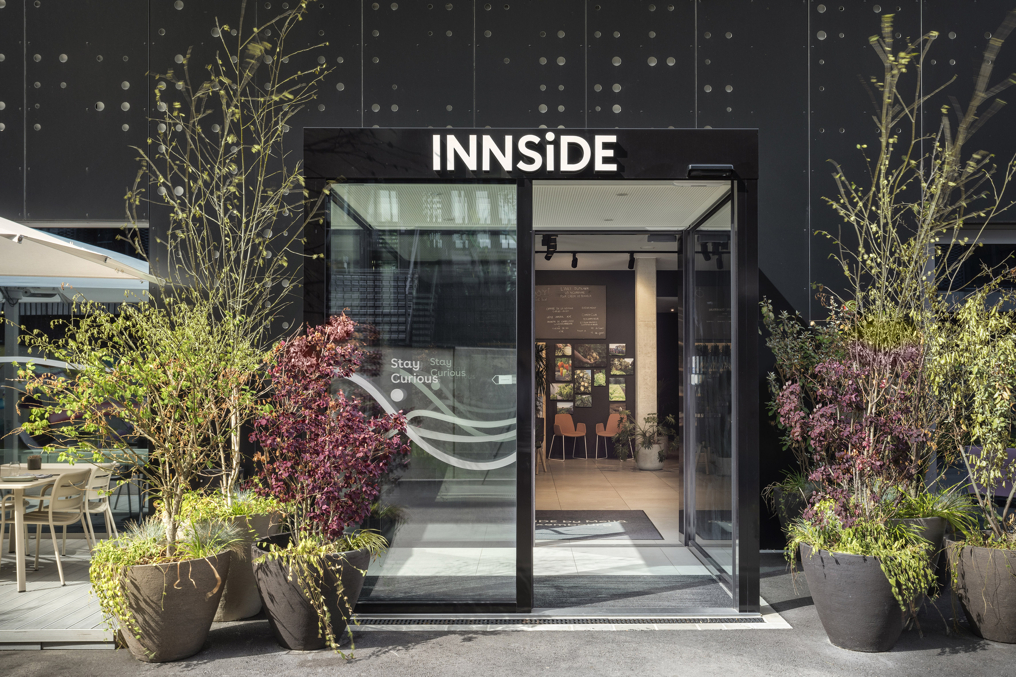 INNSIDE hotel entrance: modern glass doors, black facade, potted plants.