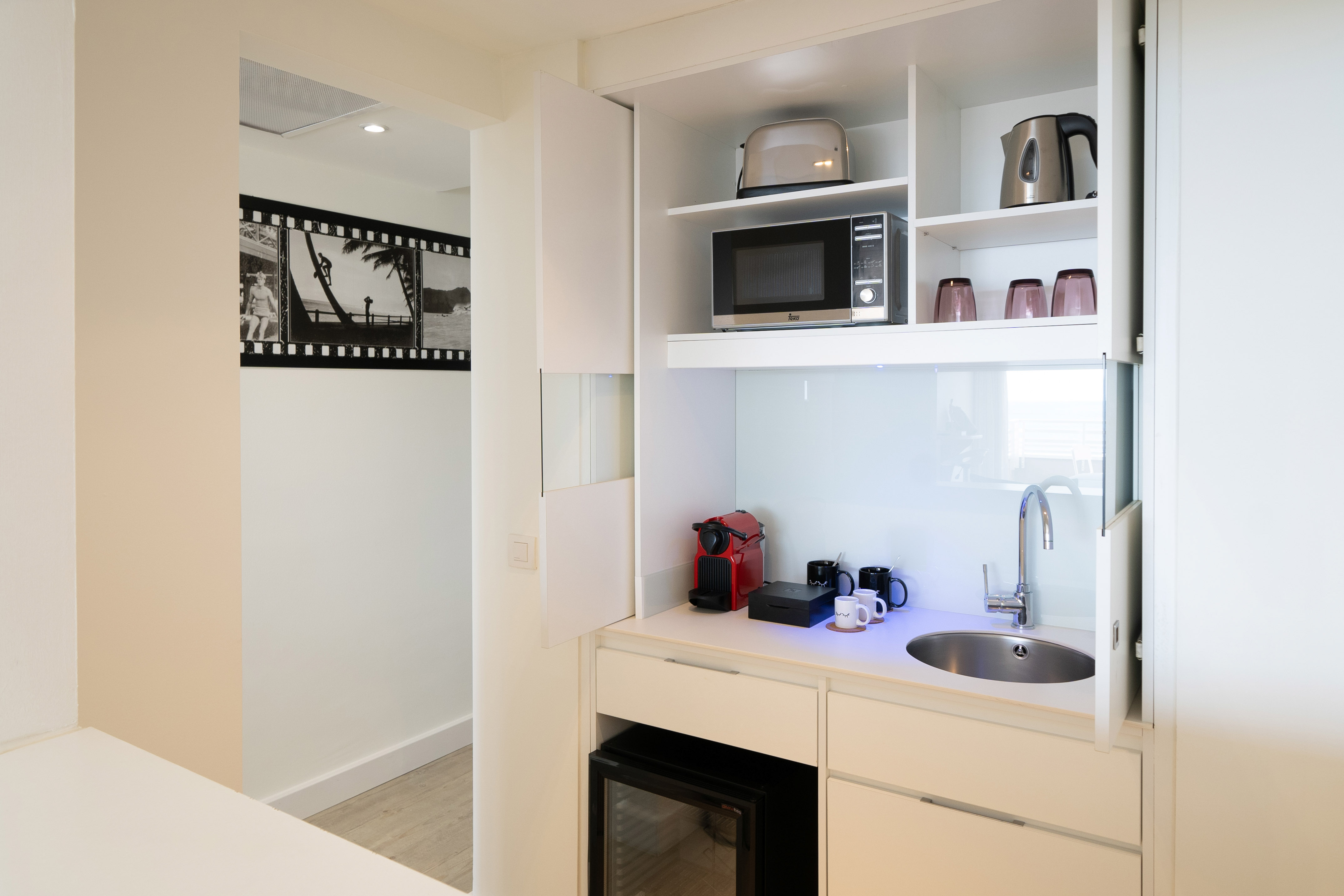 Modern hotel kitchenette with microwave, coffee machine, sink, and mini-fridge.