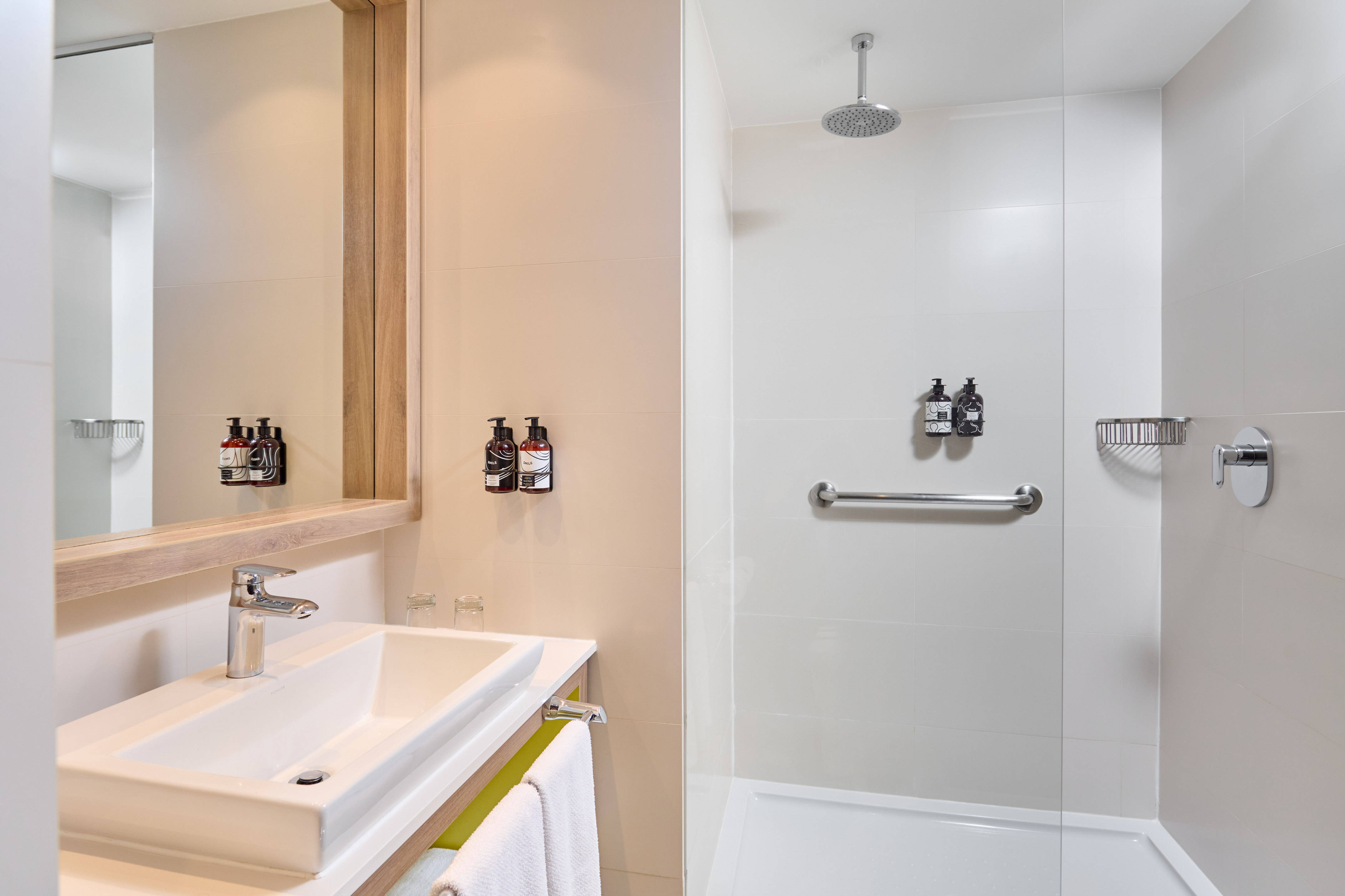 Modern hotel bathroom with white vanity, mirror, and walk-in shower.