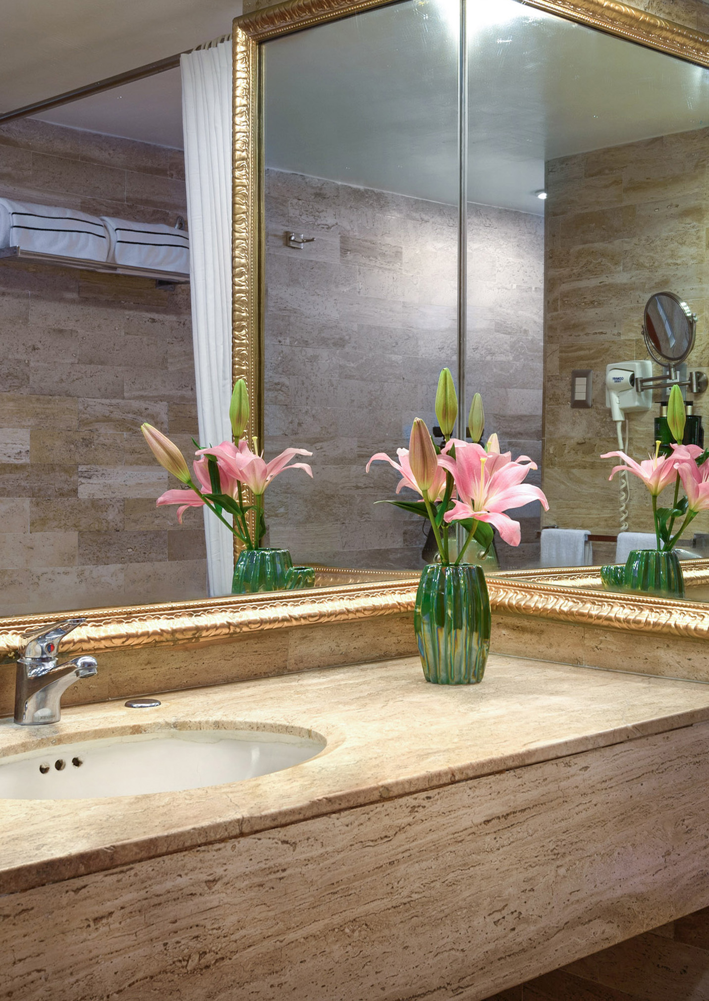 Ornate golden mirror above a stone bathroom vanity with pink lilies.