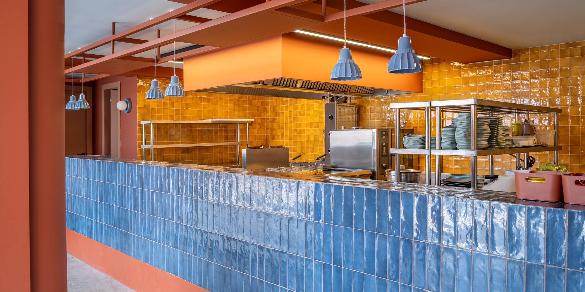 Commercial kitchen design: blue tile counter, yellow wall, steel equipment.