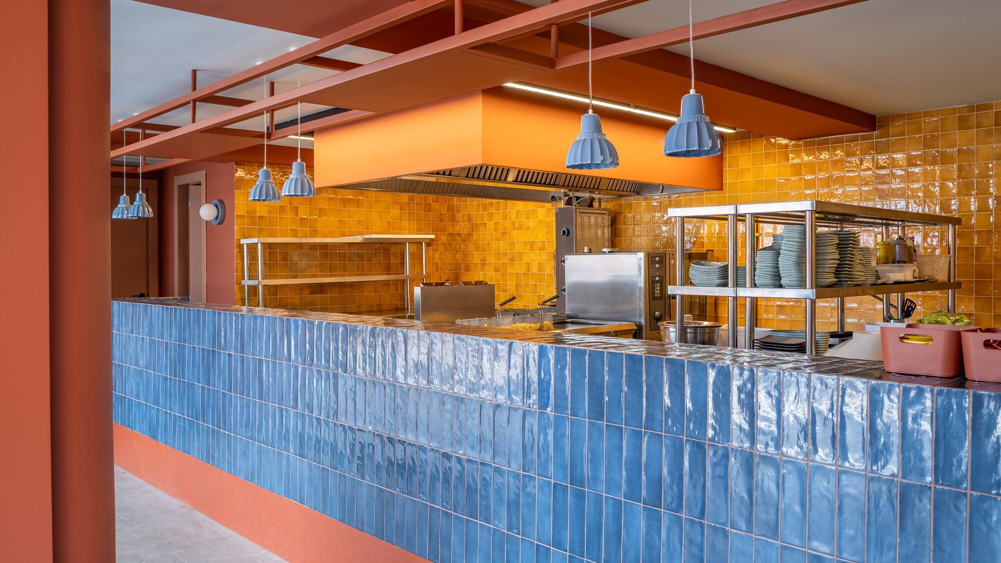 Commercial kitchen design: blue tile counter, yellow wall, steel equipment.