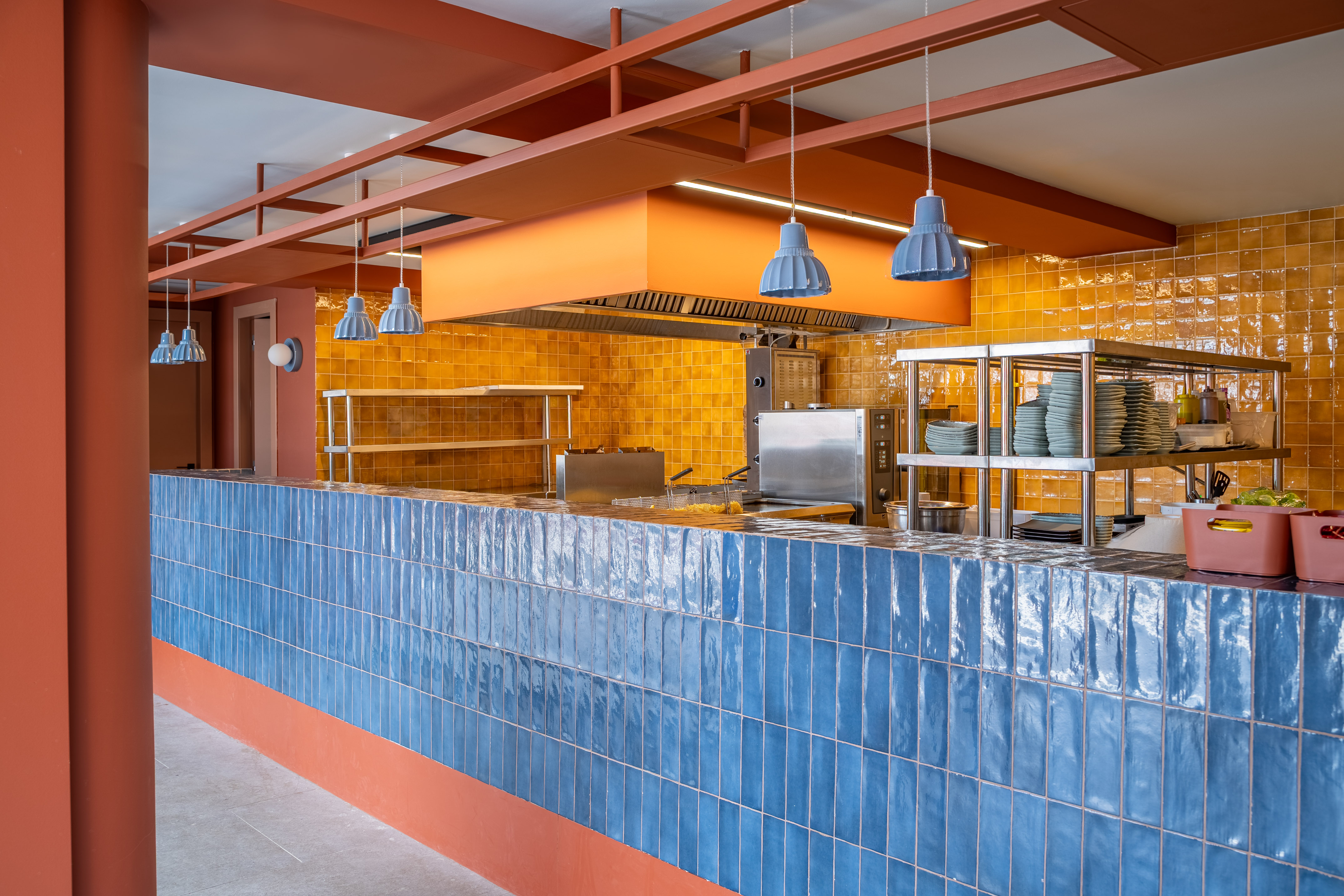 Commercial kitchen design: blue tile counter, yellow wall, steel equipment.