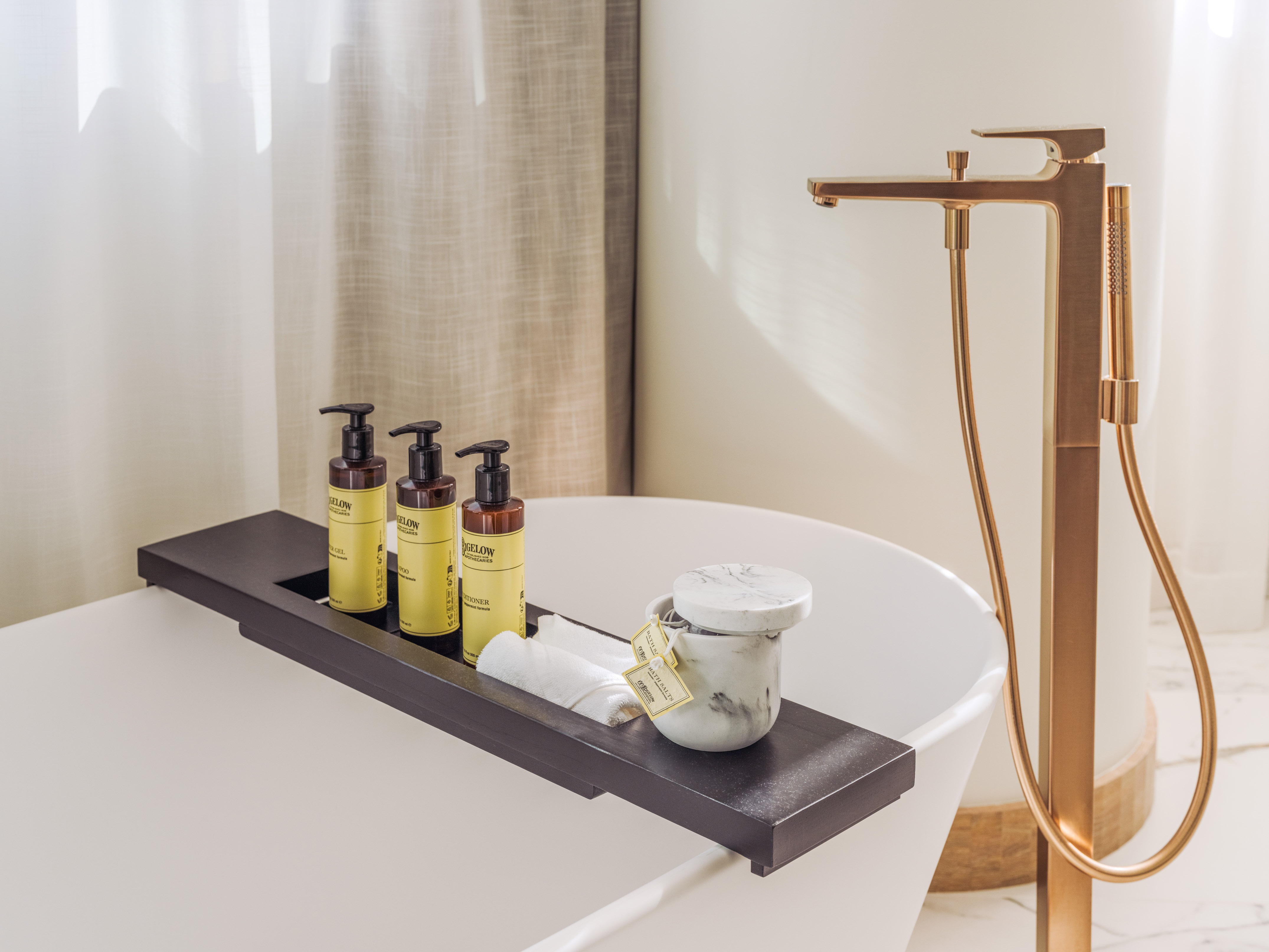 White bathtub with a dark bath caddy, bath salts, and a sleek bronze faucet.