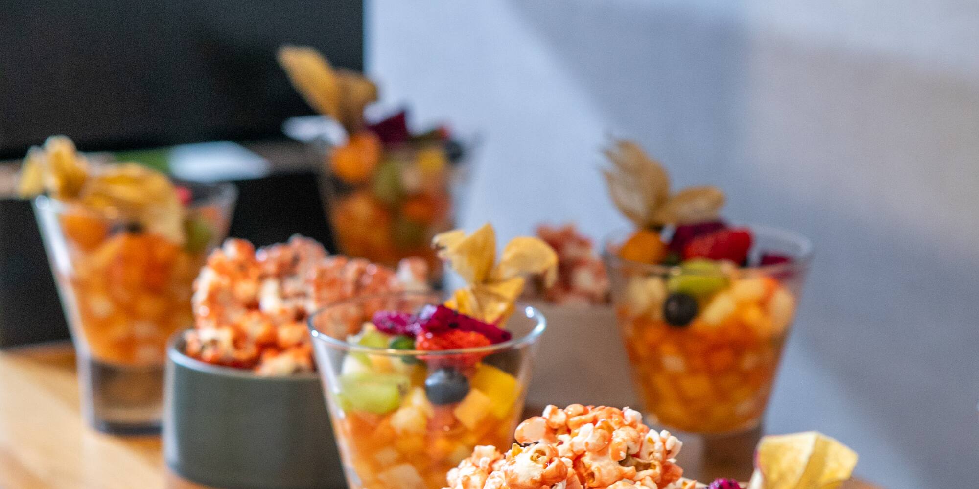 Catering display: colorful fruit salad, gourmet popcorn, and mini puff pastries.