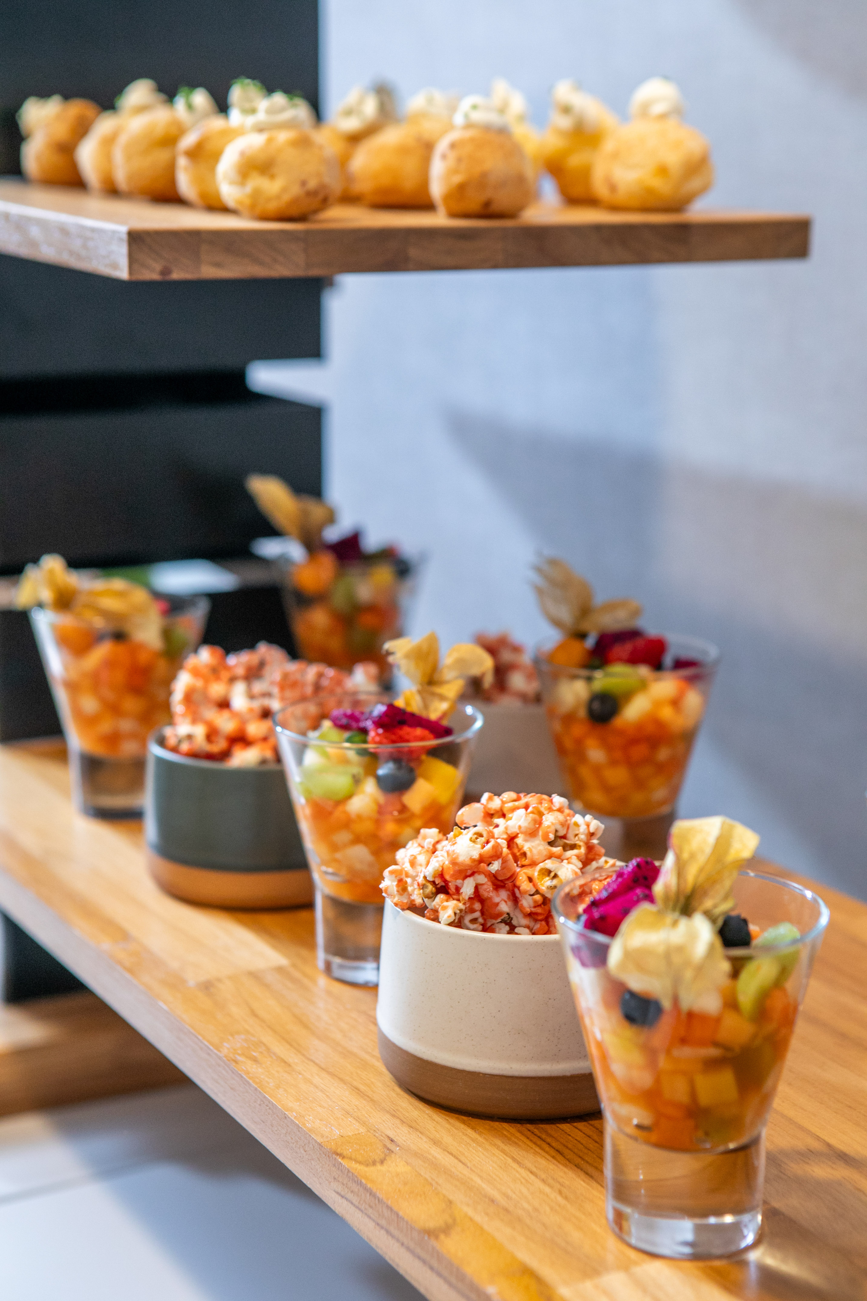 Catering display: colorful fruit salad, gourmet popcorn, and mini puff pastries.