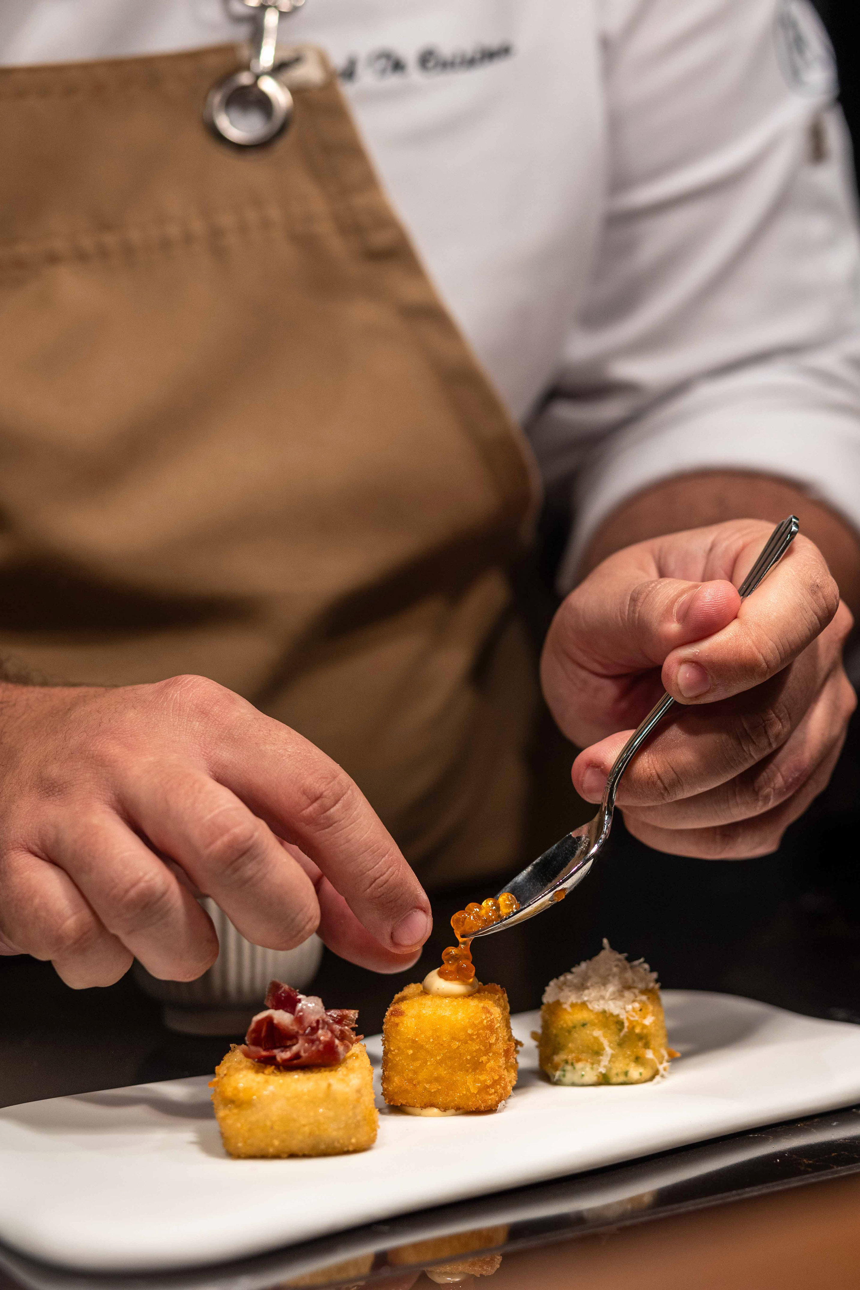Chef garnishes three croquettes with caviar, ham, and cheese. Fine dining appetizer.