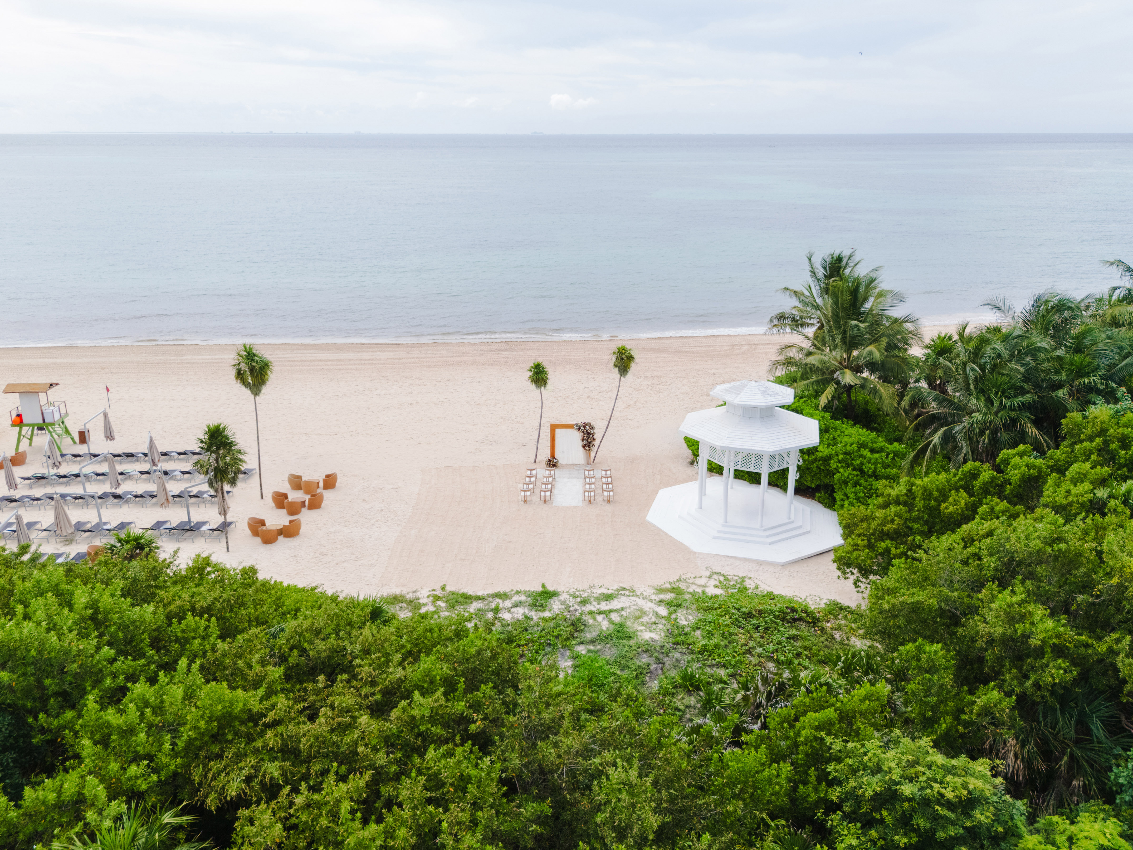 Sandy beach wedding venue with white gazebo, arch, and ocean.