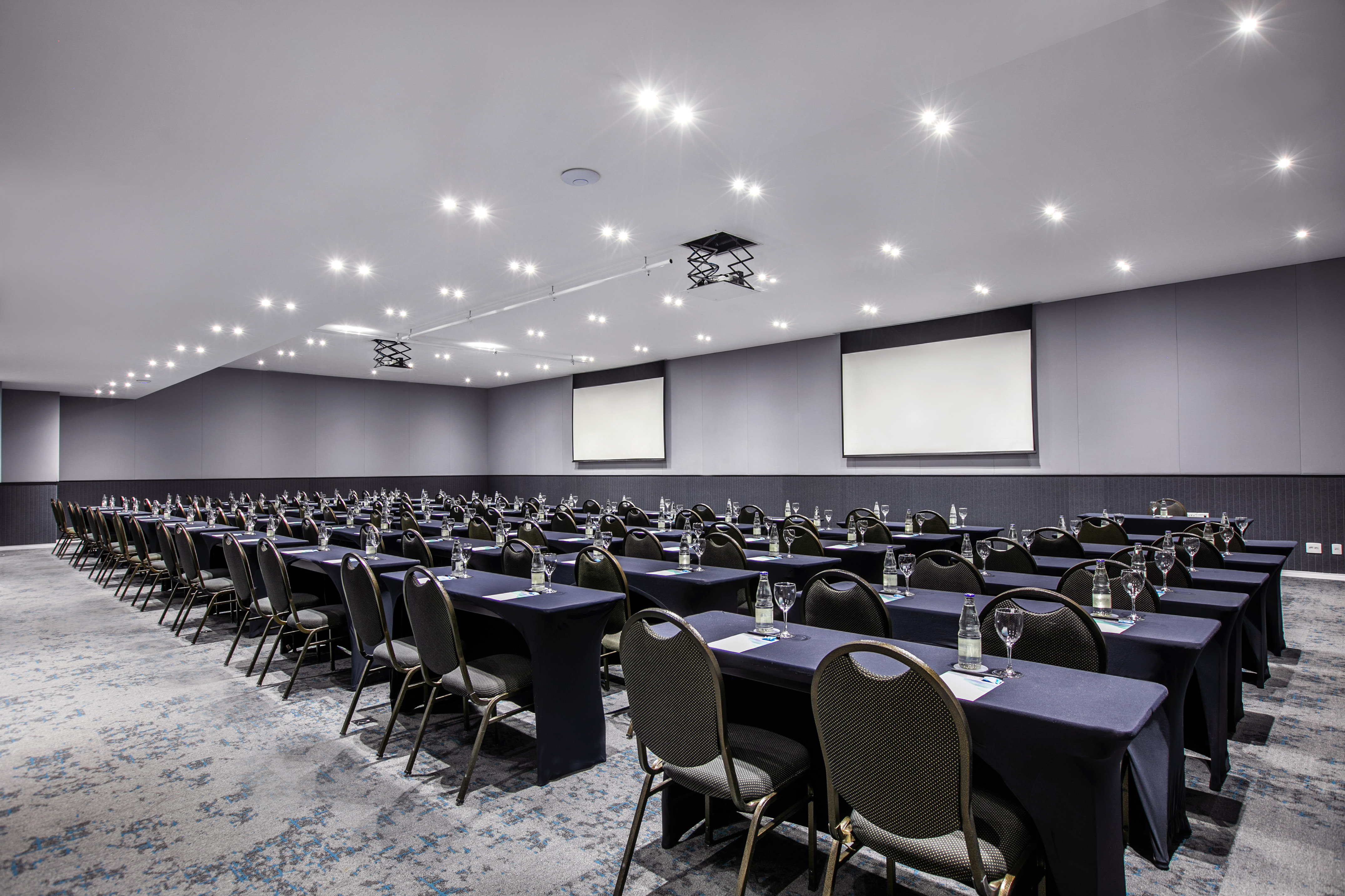 Modern conference room with classroom style tables, chairs, and dual screens.