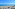 Sunny beach with blue ocean, palm trees, and coastal road.