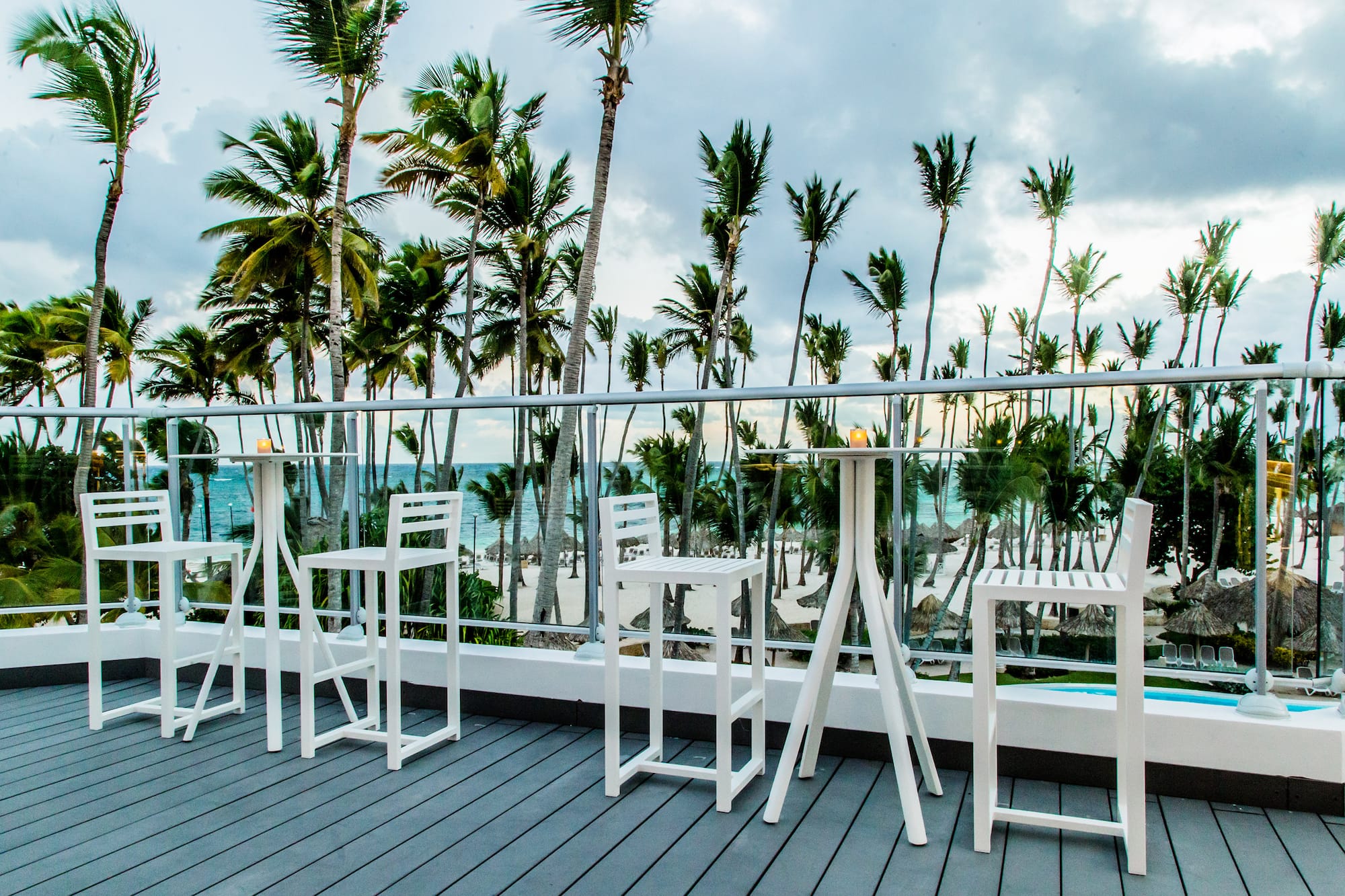 Terraza resort con bar blanco, palmeras y vista a la playa tropical.