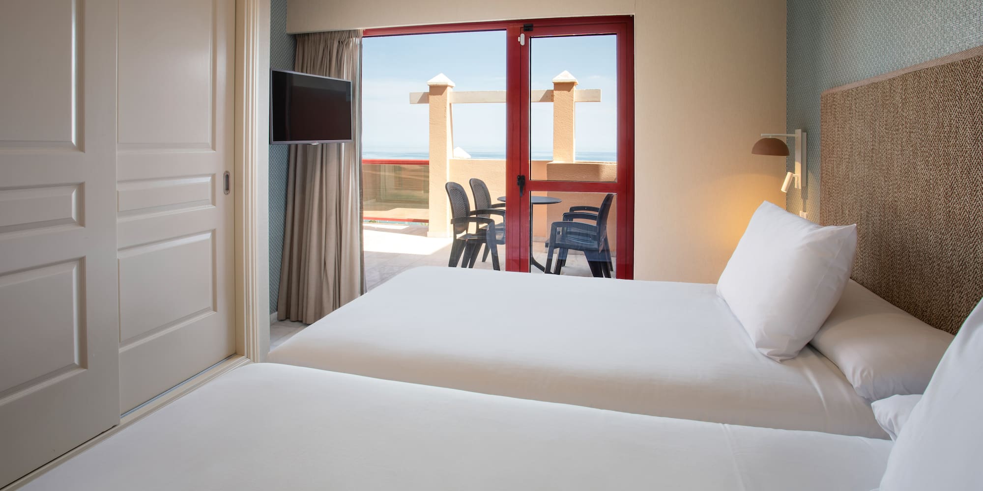 Twin hotel room with balcony, outdoor seating, and ocean view.