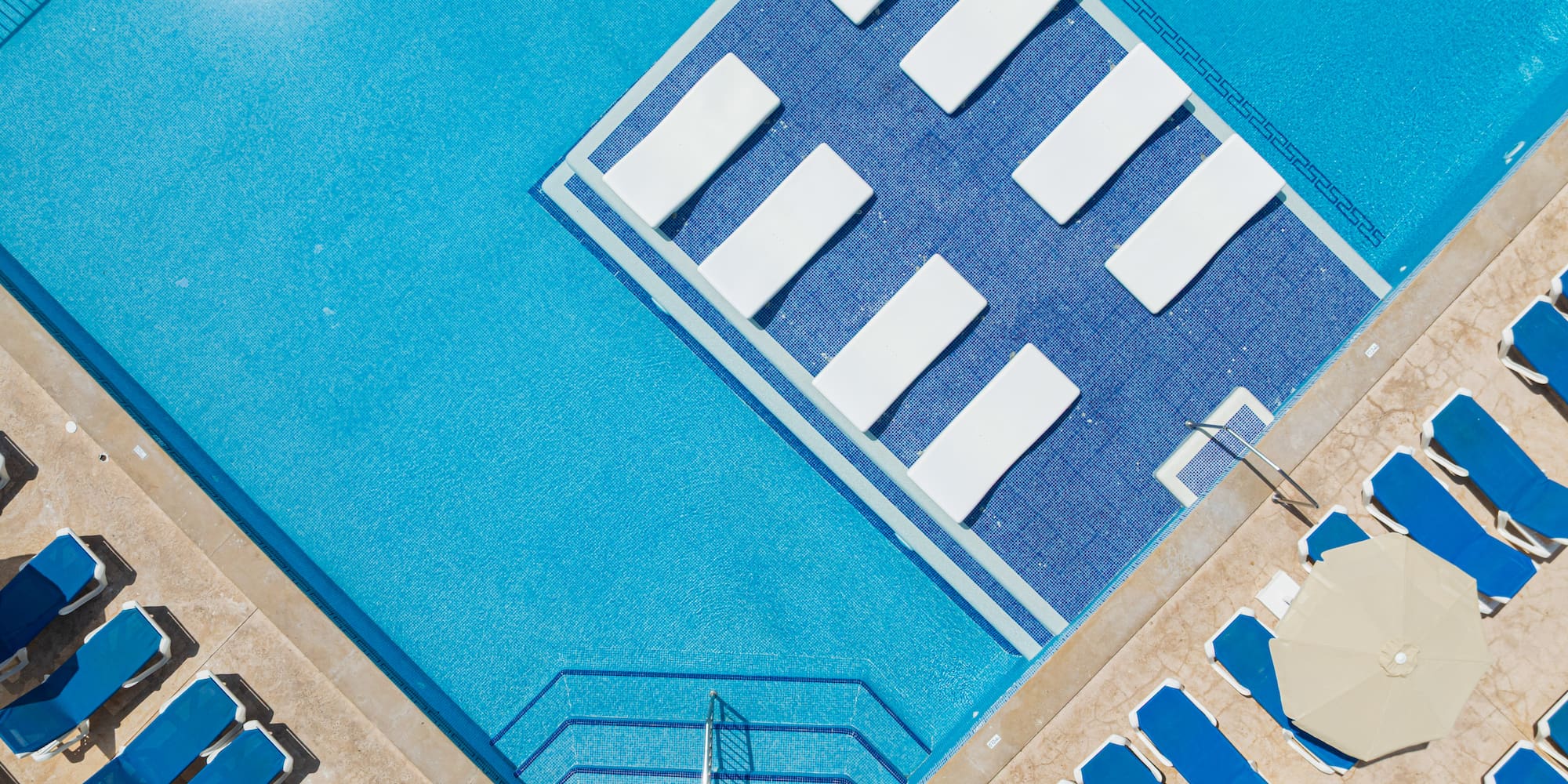 Aerial view bright blue resort swimming pool with sun loungers and umbrellas.
